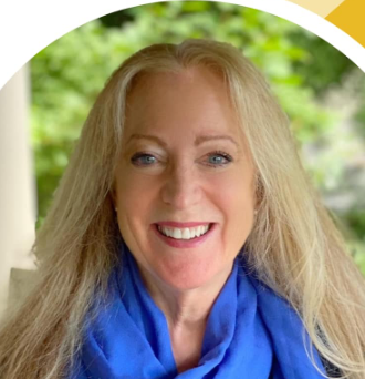 Portrait of a smiling woman with long blonde hair and a blue scarf, outdoors with greenery in the background.