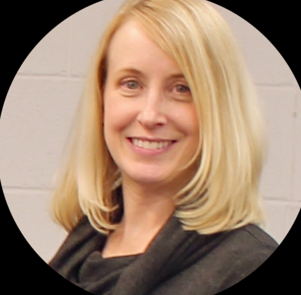 Smile of a blonde woman with shoulder-length hair, standing in front of a brick wall.