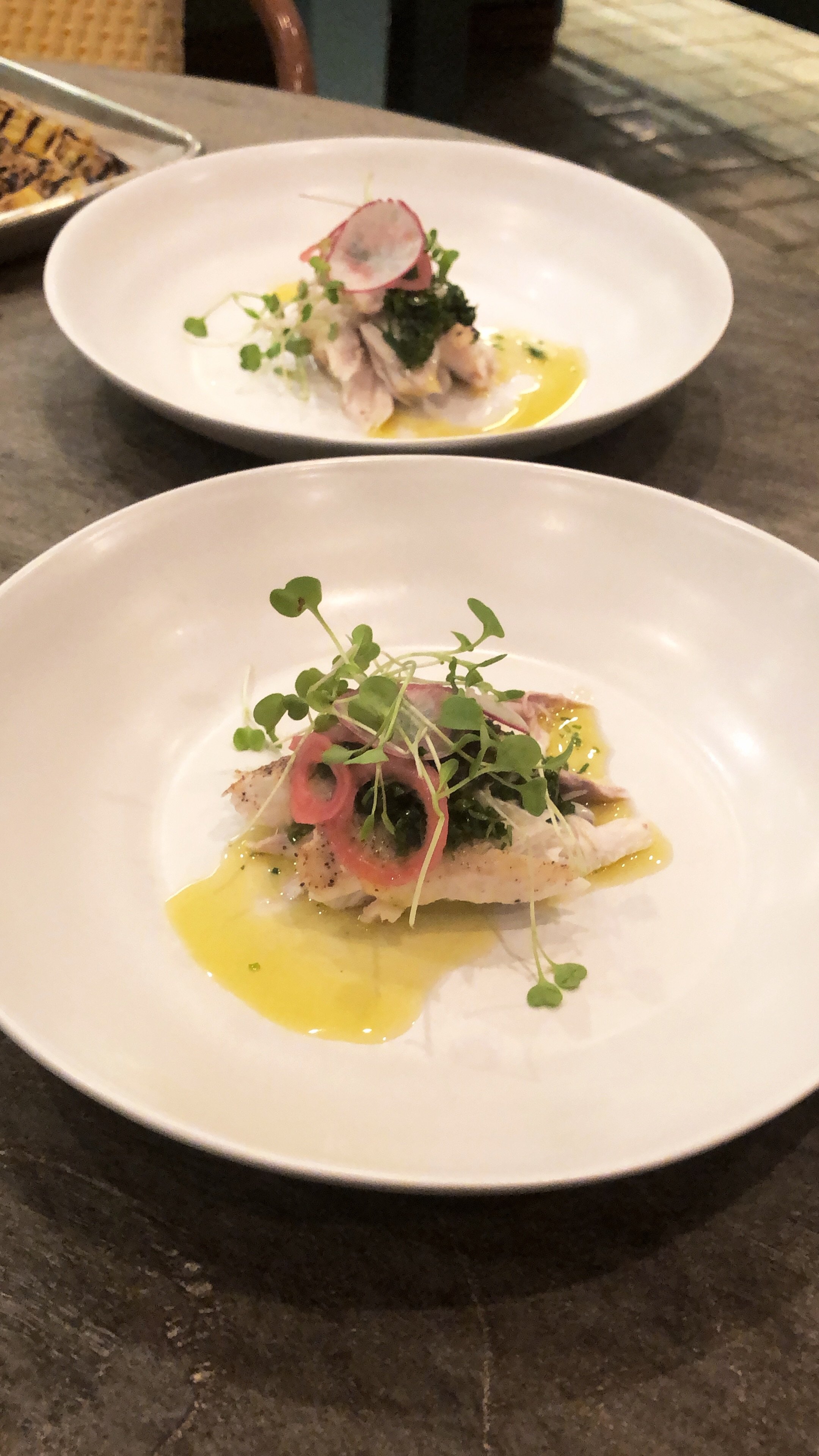 Gourmet dish with fish, microgreens, pickled onions in white bowls on a table.