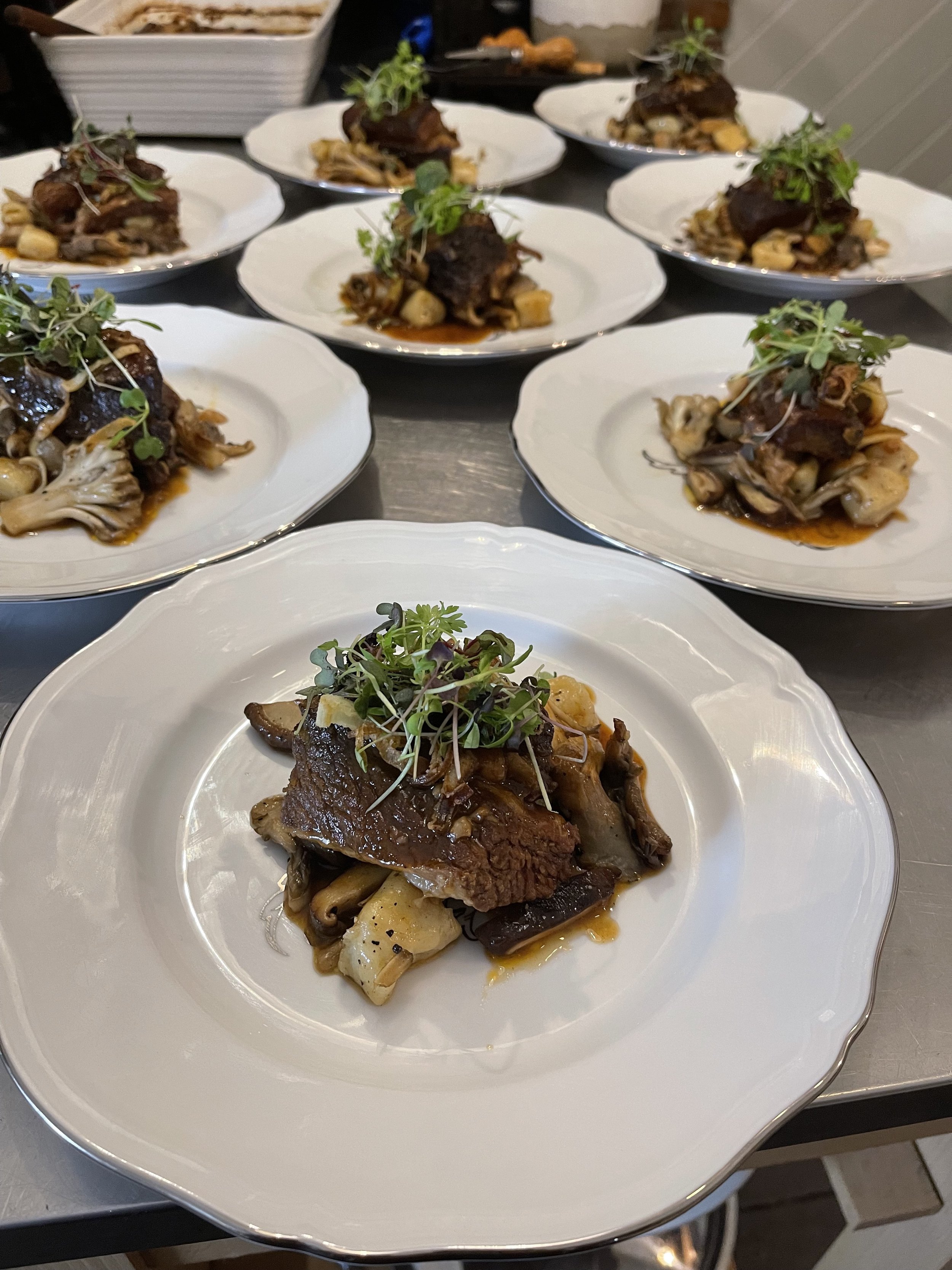Plates of braised beef with mushrooms and microgreens on a table.