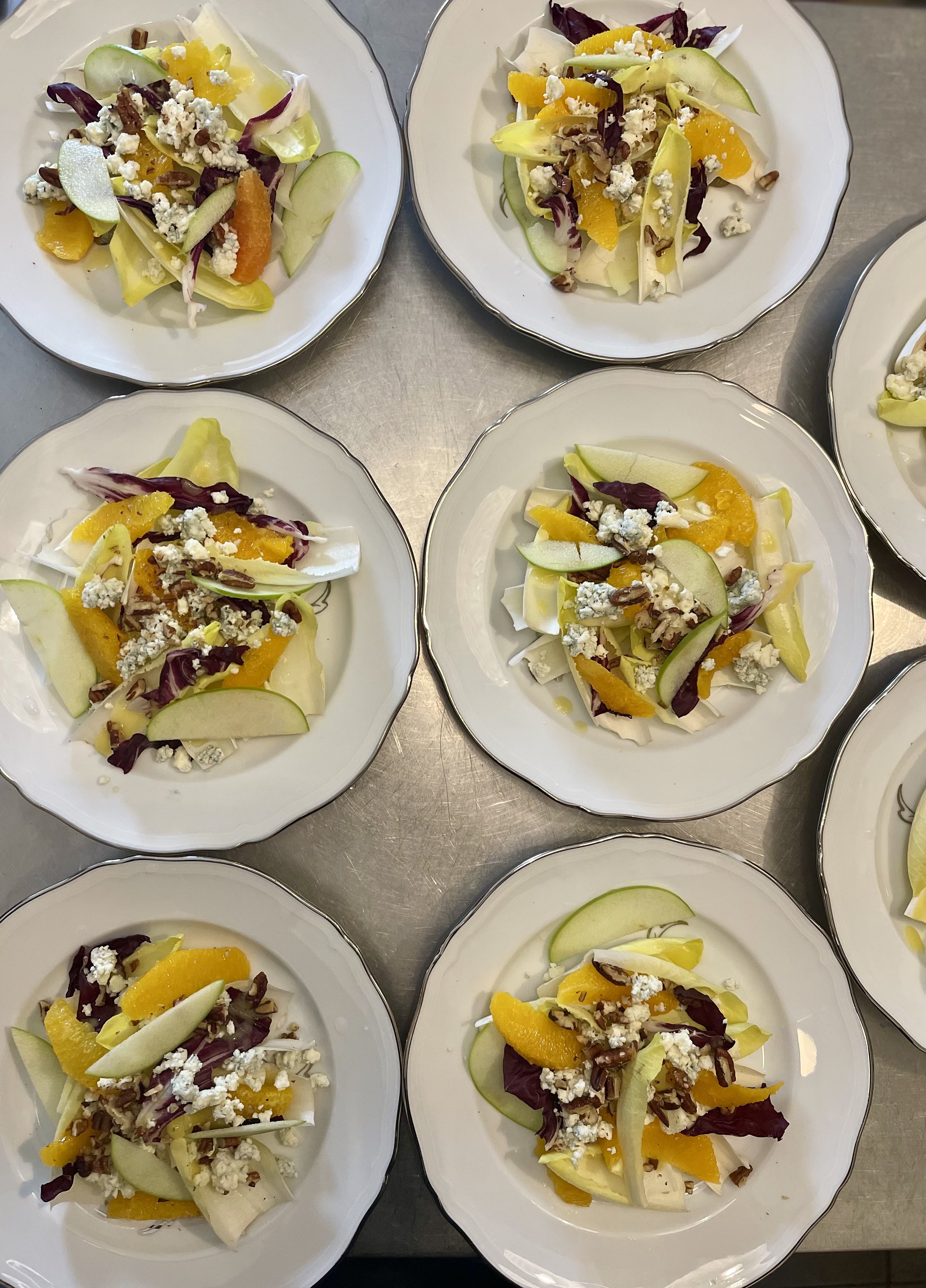 Plates with salad containing apple slices, orange segments, crumbled cheese, radicchio, and endive.