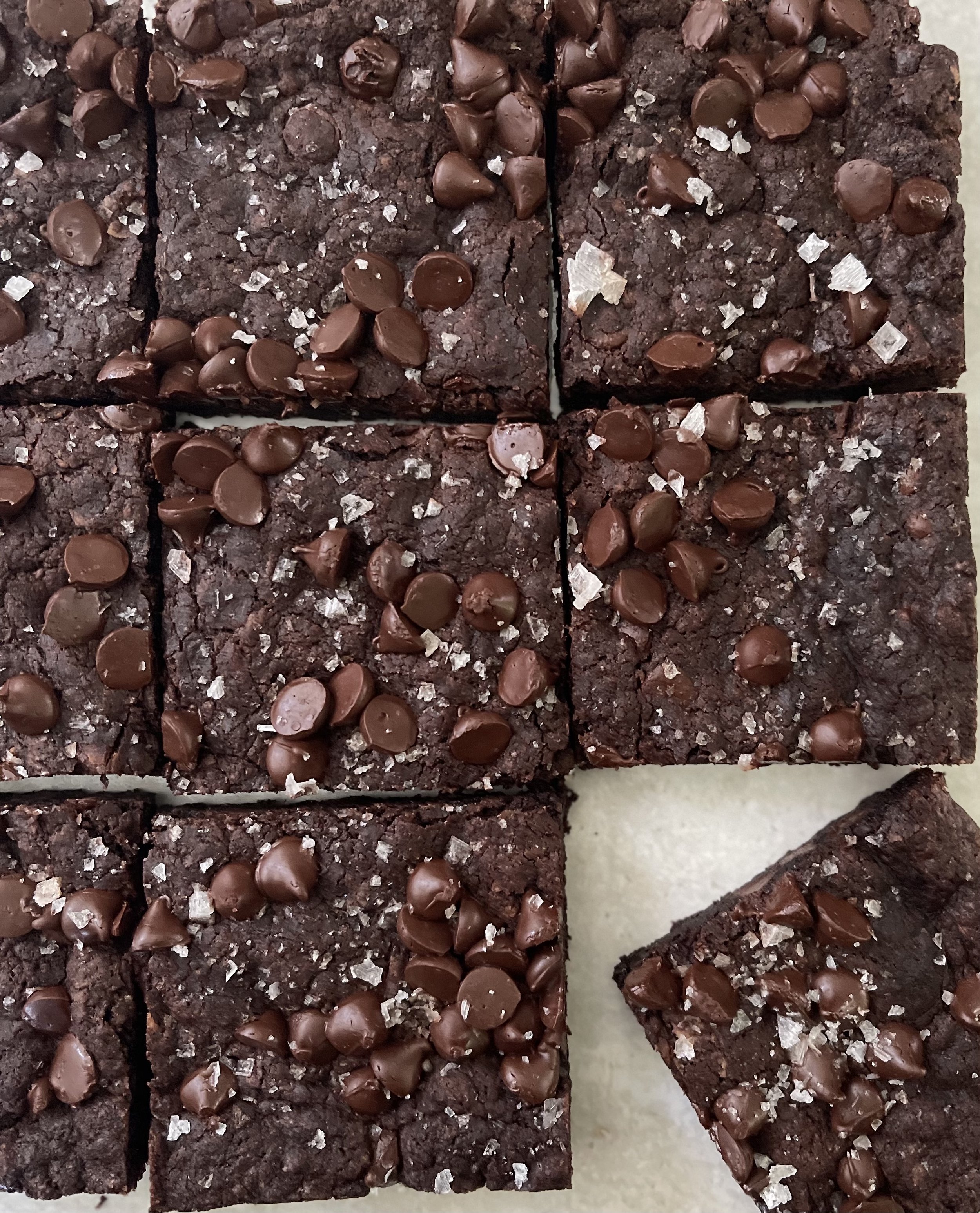 Close-up of chocolate brownies topped with chocolate chips and sea salt, cut into squares.