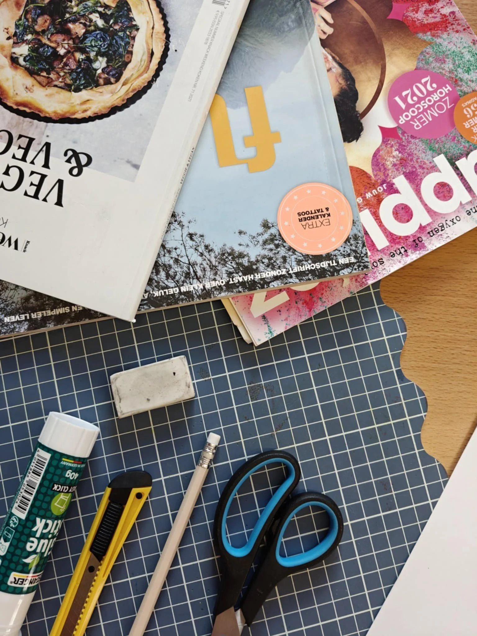 Kantoorwerkplek met een snijder, een lijmstok, een potlood, een stuk gum, een paar scharen en tijdschriften op een tafel