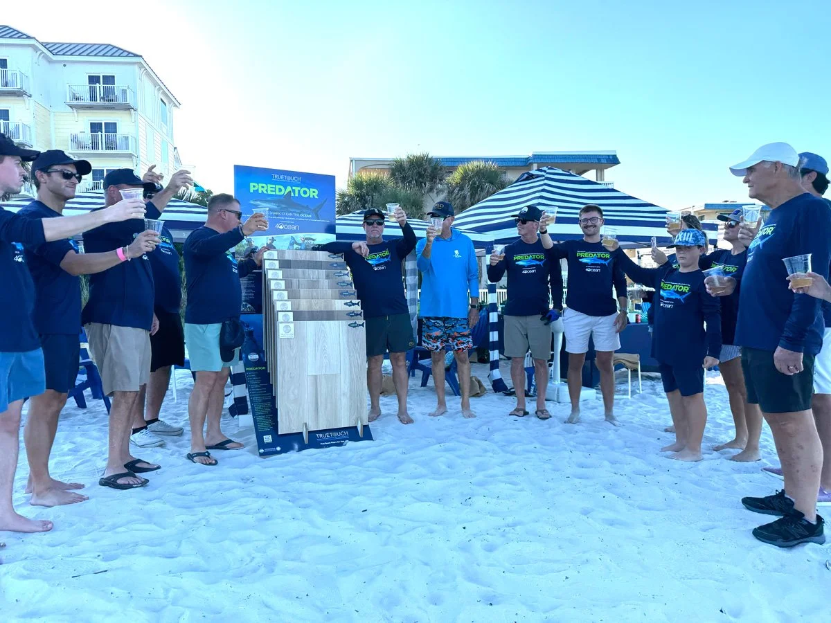 TrueTouch people wearing 4ocean Predator shirts standing next to a MonoTeech Predator floor display on the beach