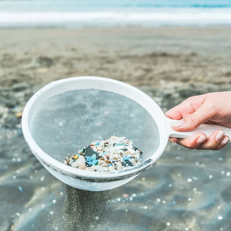 a hand holding a strainer filled with microplastics from the ocean