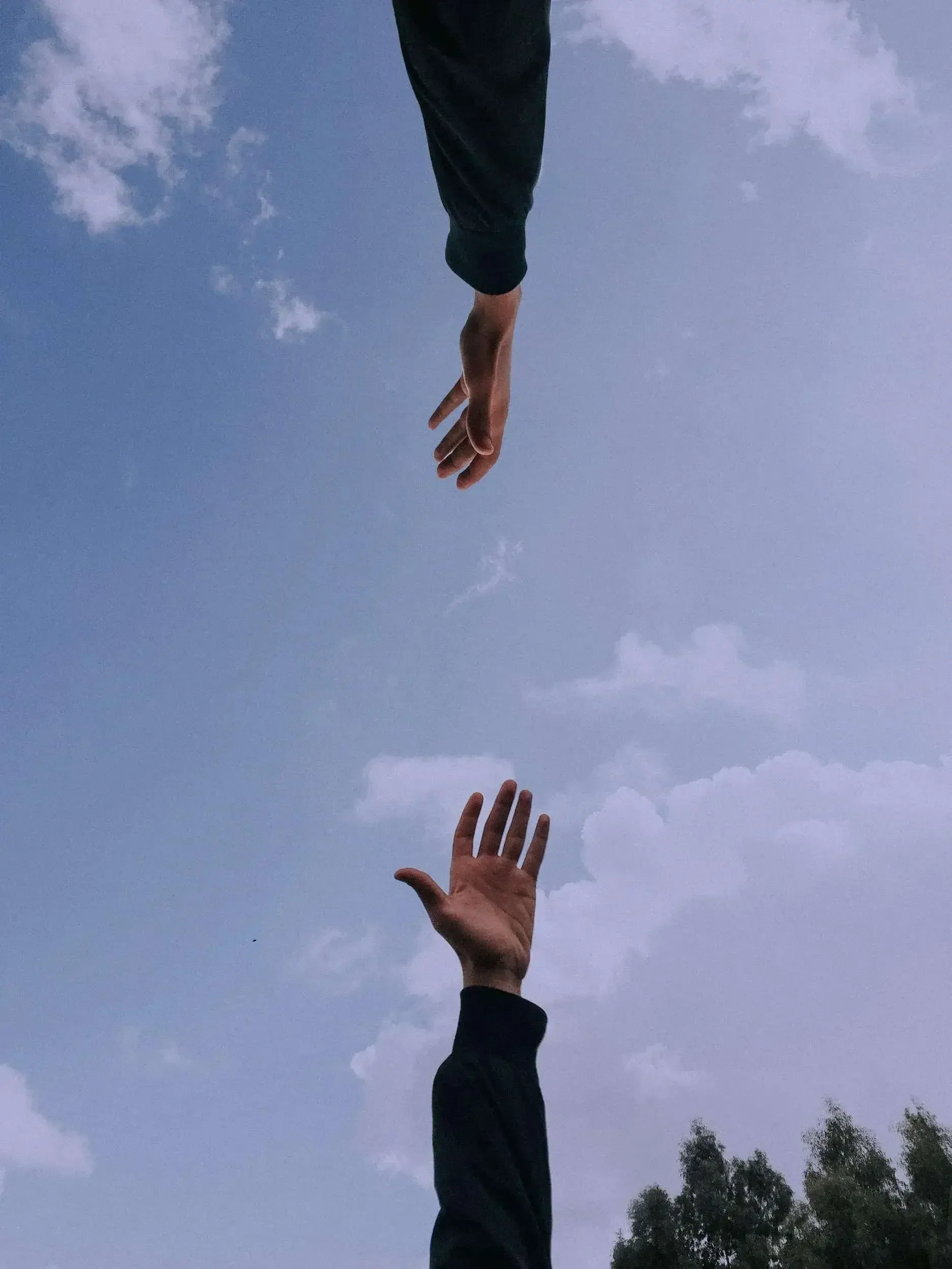 Two hands reaching towards each other against a blue sky with clouds.