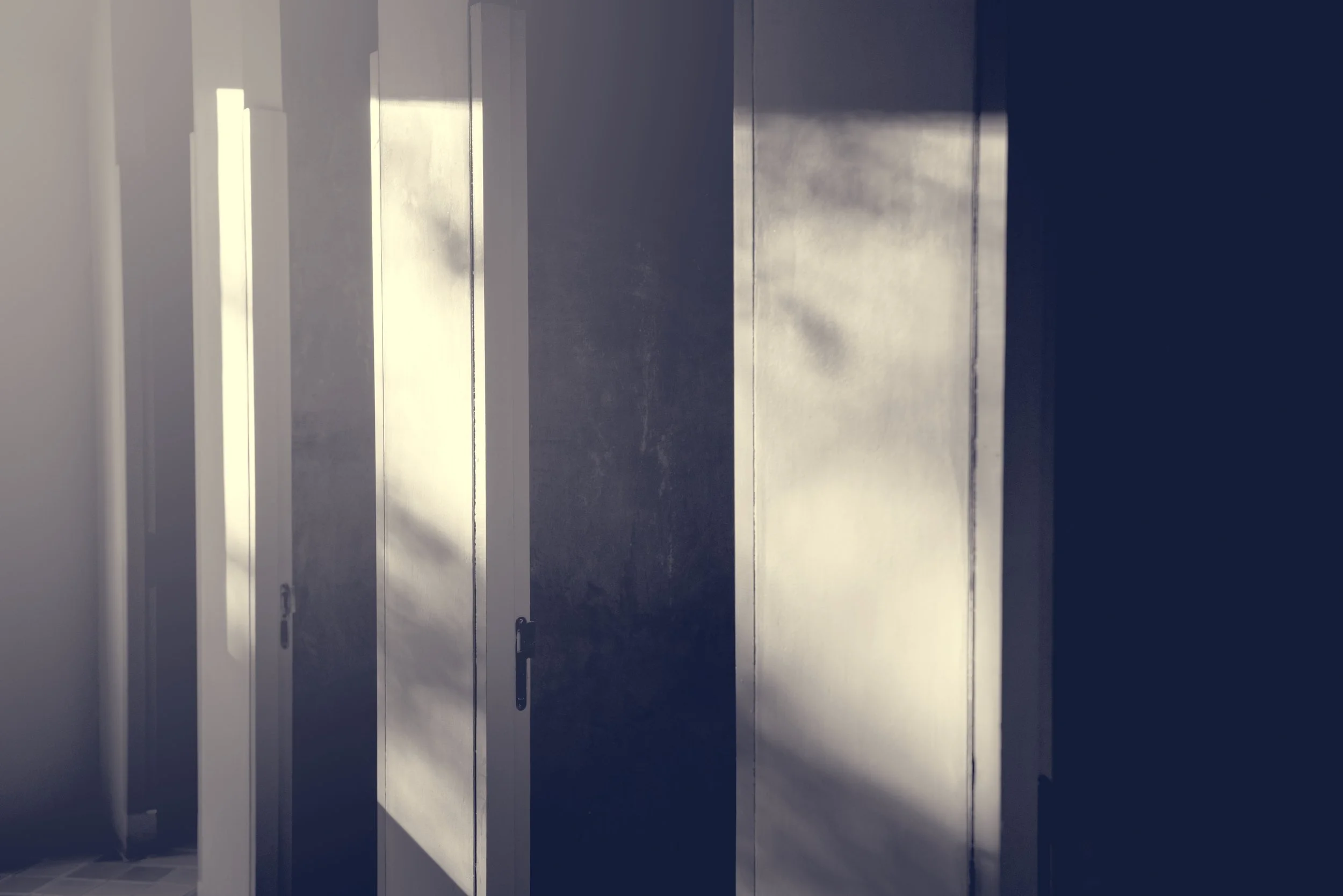 Empty stalls with closed white doors and metal handles, partially illuminated with sunlight.