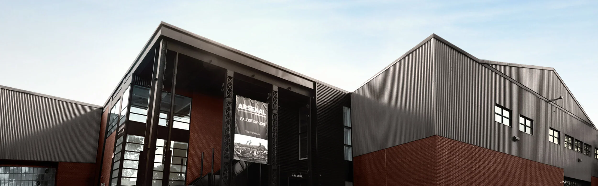 Vue extérieure d'un bâtiment moderne avec une façade en métal et en briques, affichant une bannière publicitaire pour un centre d'art.