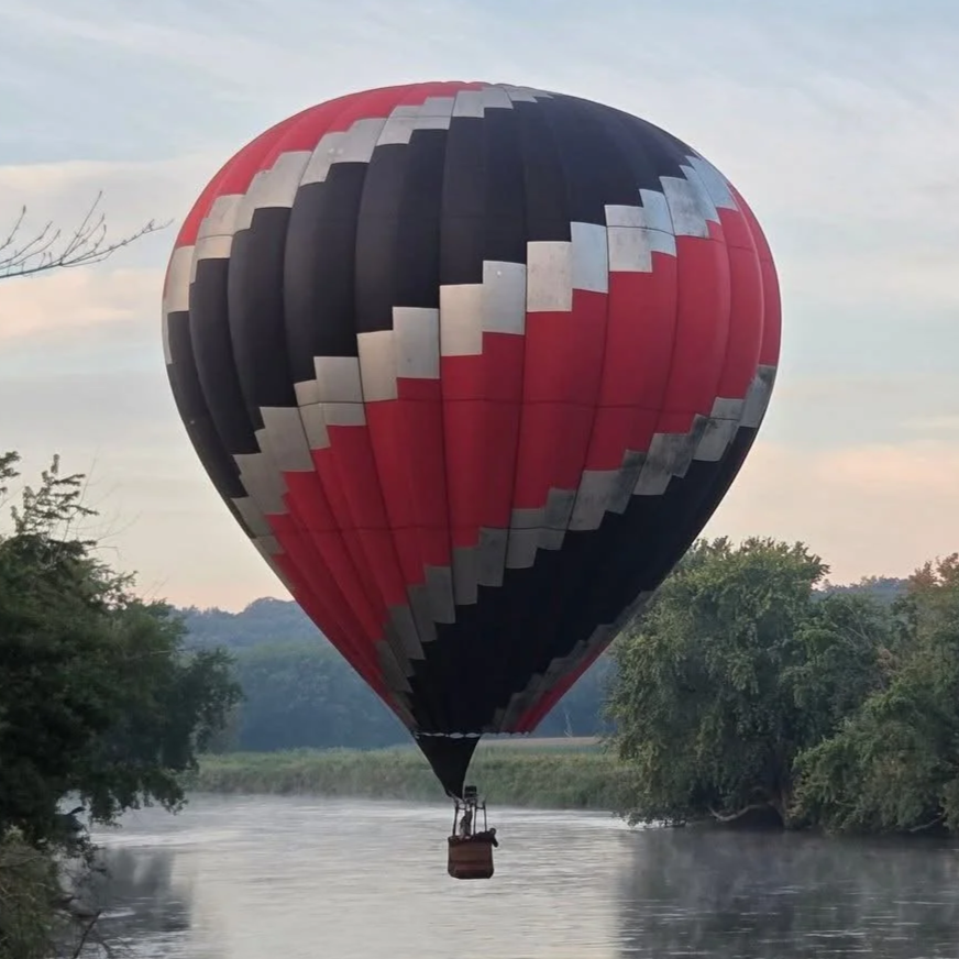 Colorful hot air balloon with a black, red, and silver geometric spiral pattern floating in the sky.
