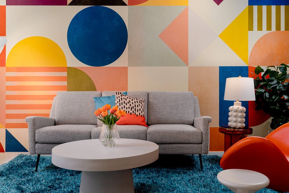 Querencia Palms Unit 102 living room in Palm Springs with a gray sofa, blue rug, and colorful geometric wallpaper.