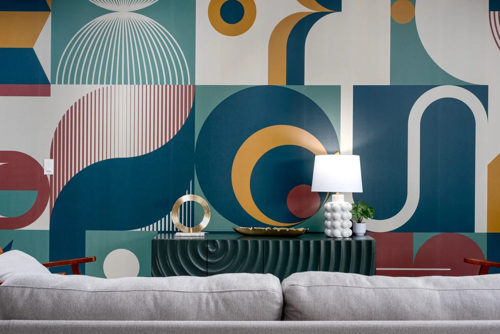 Querencia Palms Unit 105 in Palm Springs, with a green credenza and blue, pink, and gold geometric wallpaper behind a gray sofa.