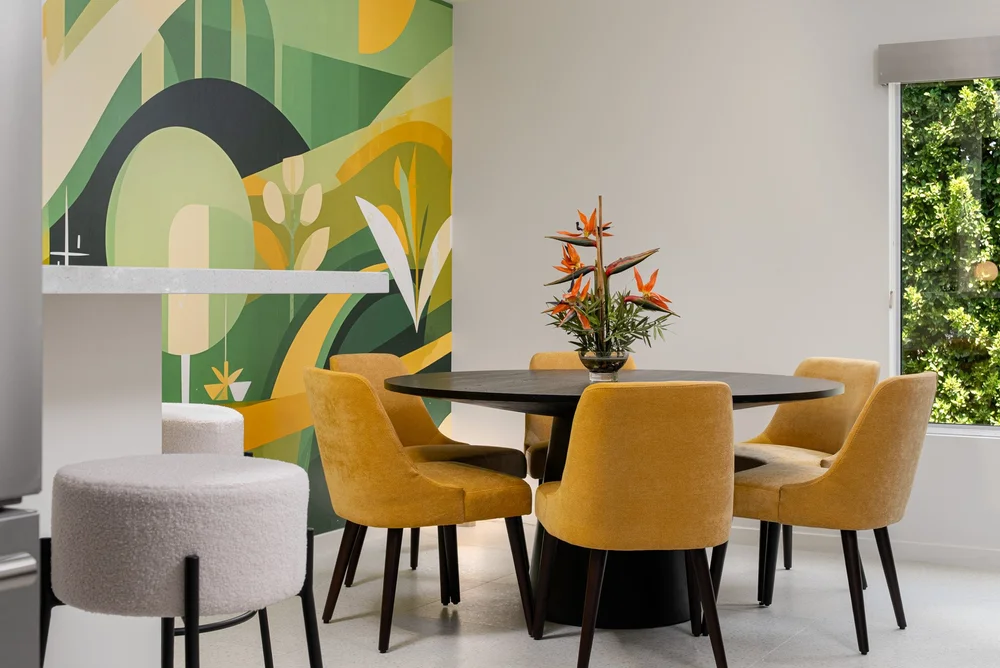 Dining area in Querencia Palms Unit 206, Palm Springs, with a round black table, mustard-colored chairs, and green-and-yellow wallpaper.