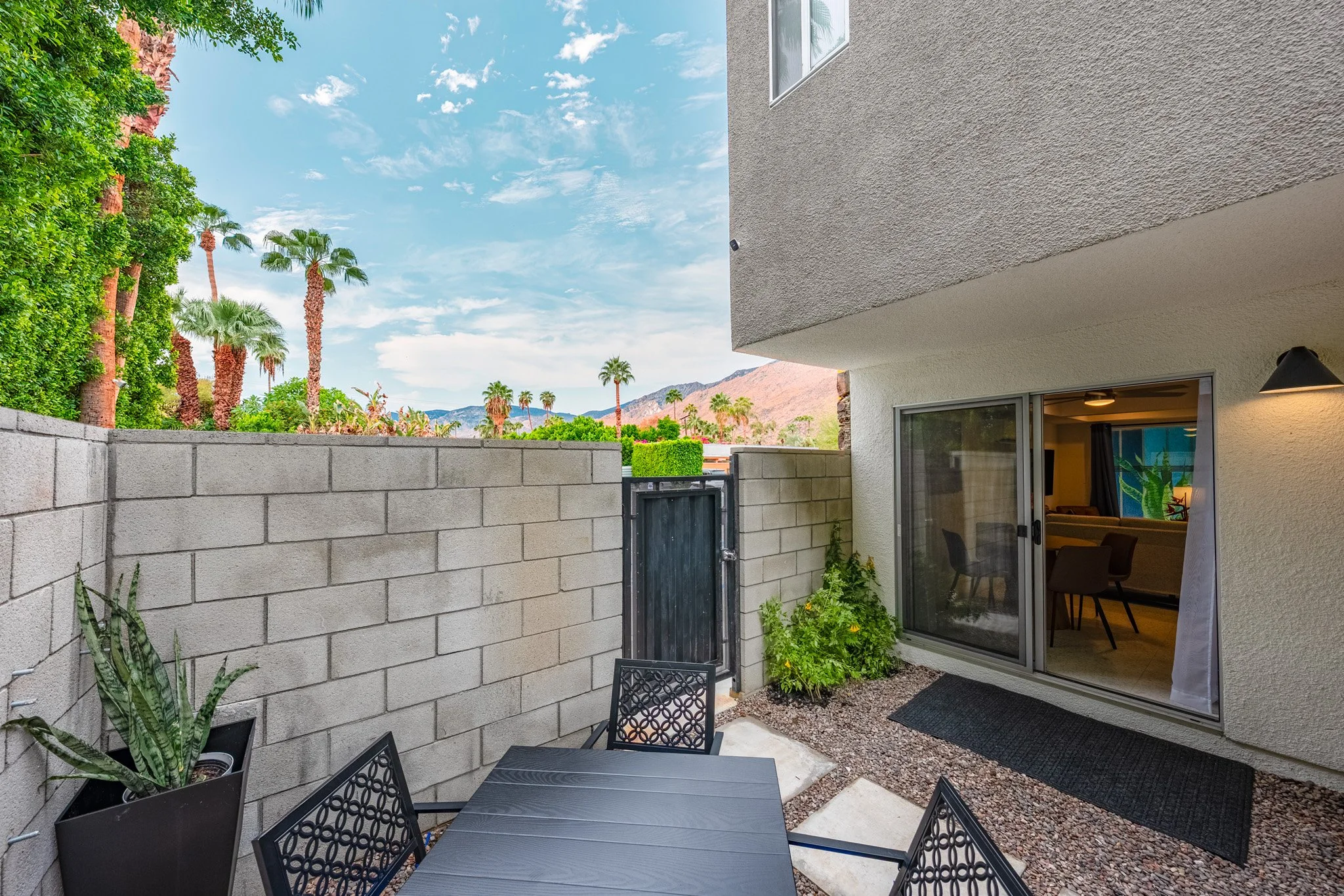 Private gated patio at Querencia Palms Unit 107 in Palm Springs with outdoor dining, desert landscaping, mountain views, and sliding glass doors.