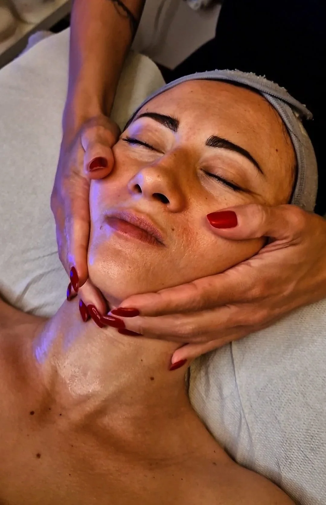 Una donna riceve un massaggio al viso, con gli occhi chiusi e un'espressione rilassata.