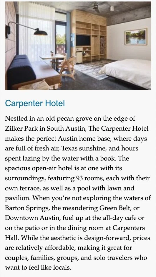 Interior of a hotel room with a bed, a built-in wooden shelving unit, a small dining table with chairs, a large window with curtains, and a painting on the wall.