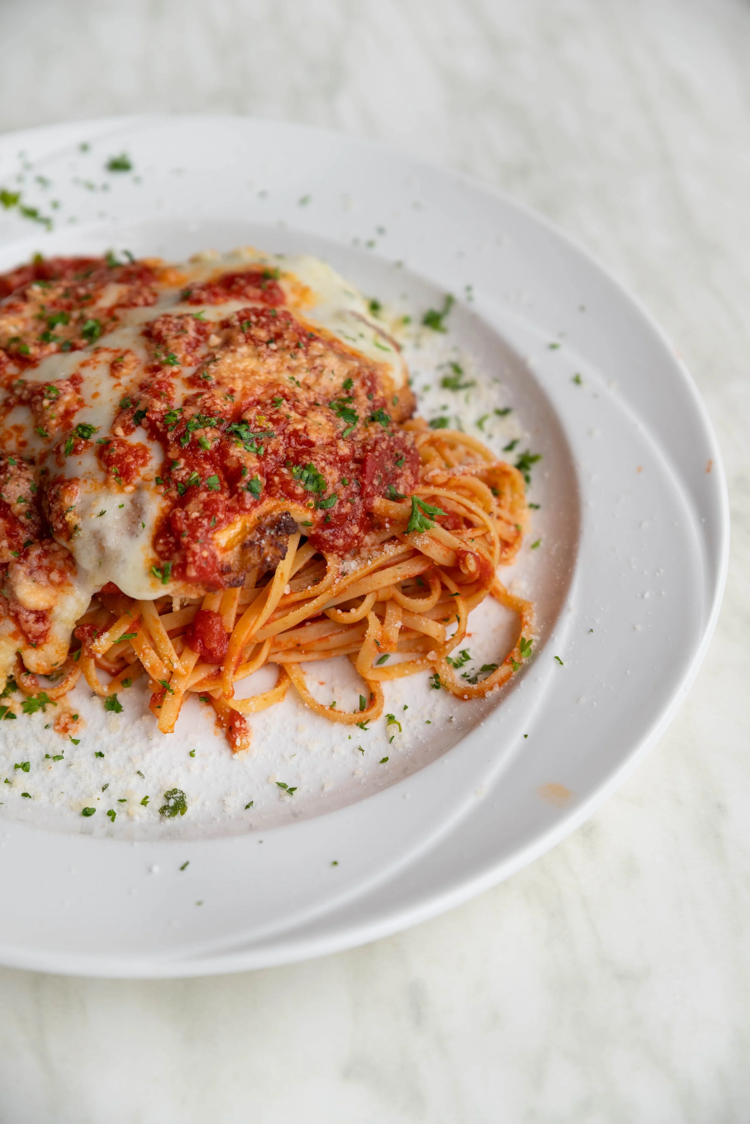 Plate of spaghetti with tomato sauce, melted cheese, and chopped parsley garnish