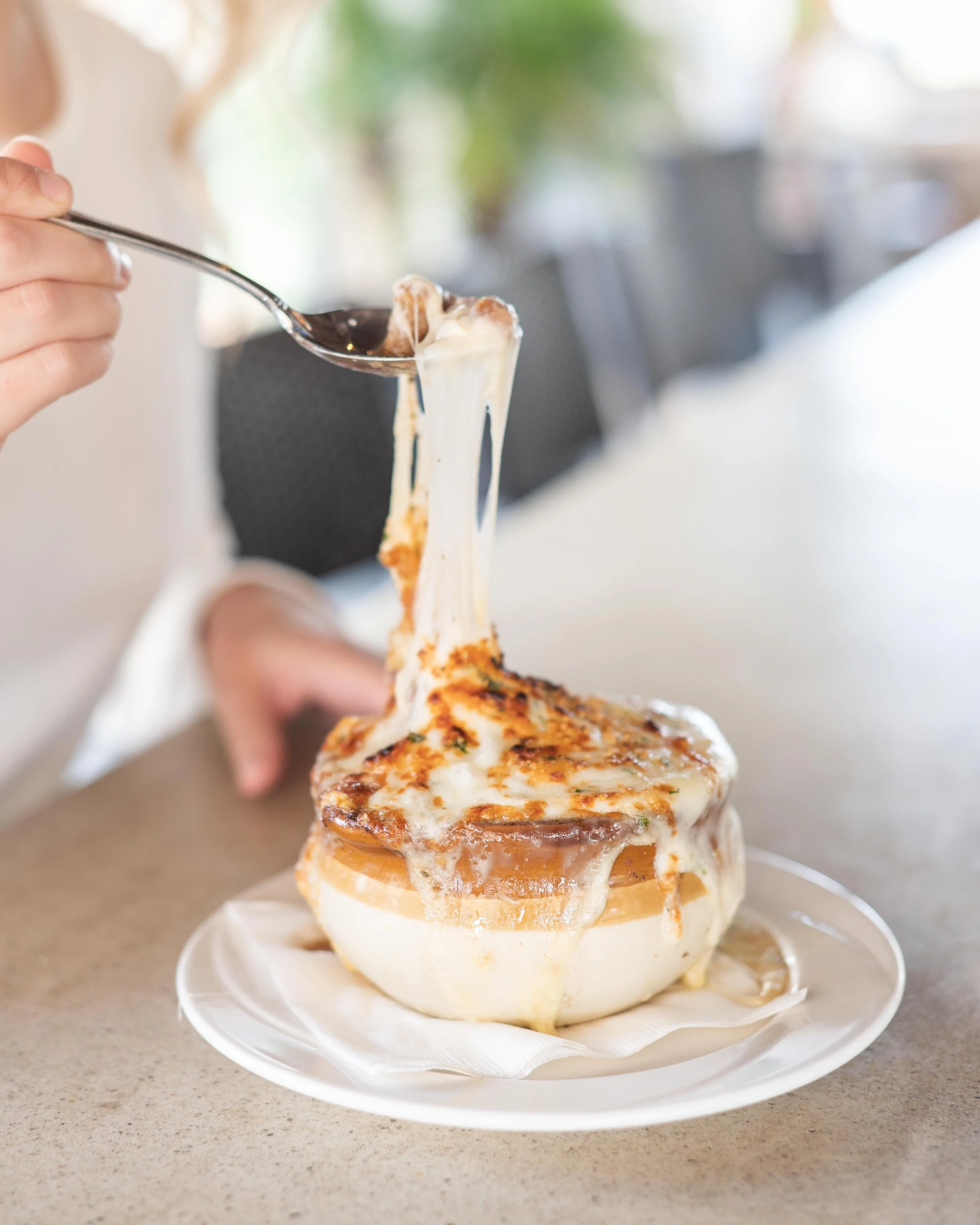 Person scooping cheesy, baked casserole from a bread bowl with a spoon.