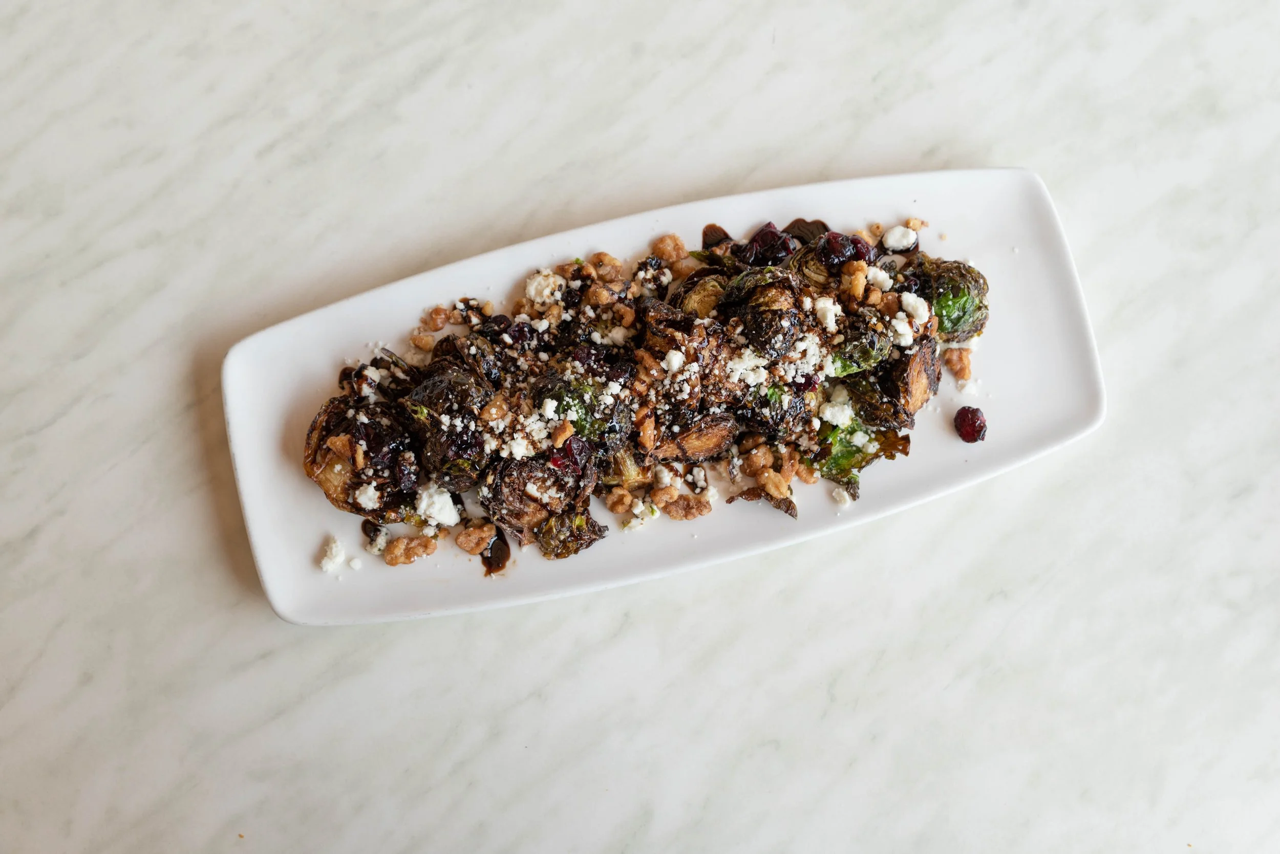 Roasted Brussels sprouts with crumbled cheese, nuts, and dried berries on a white rectangular plate