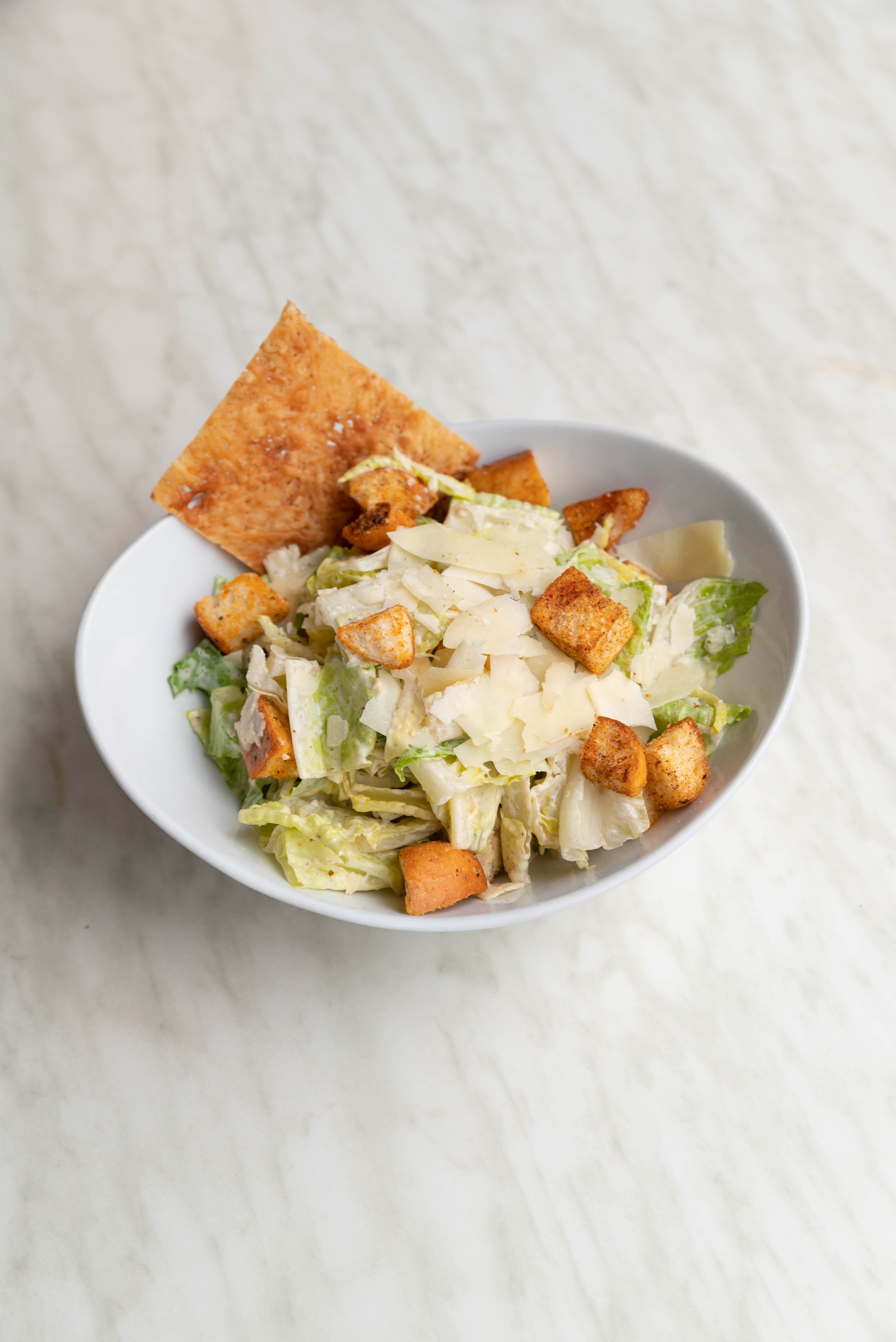 A bowl of Caesar salad topped with grated cheese, croutons, and a large crisp bread chip.