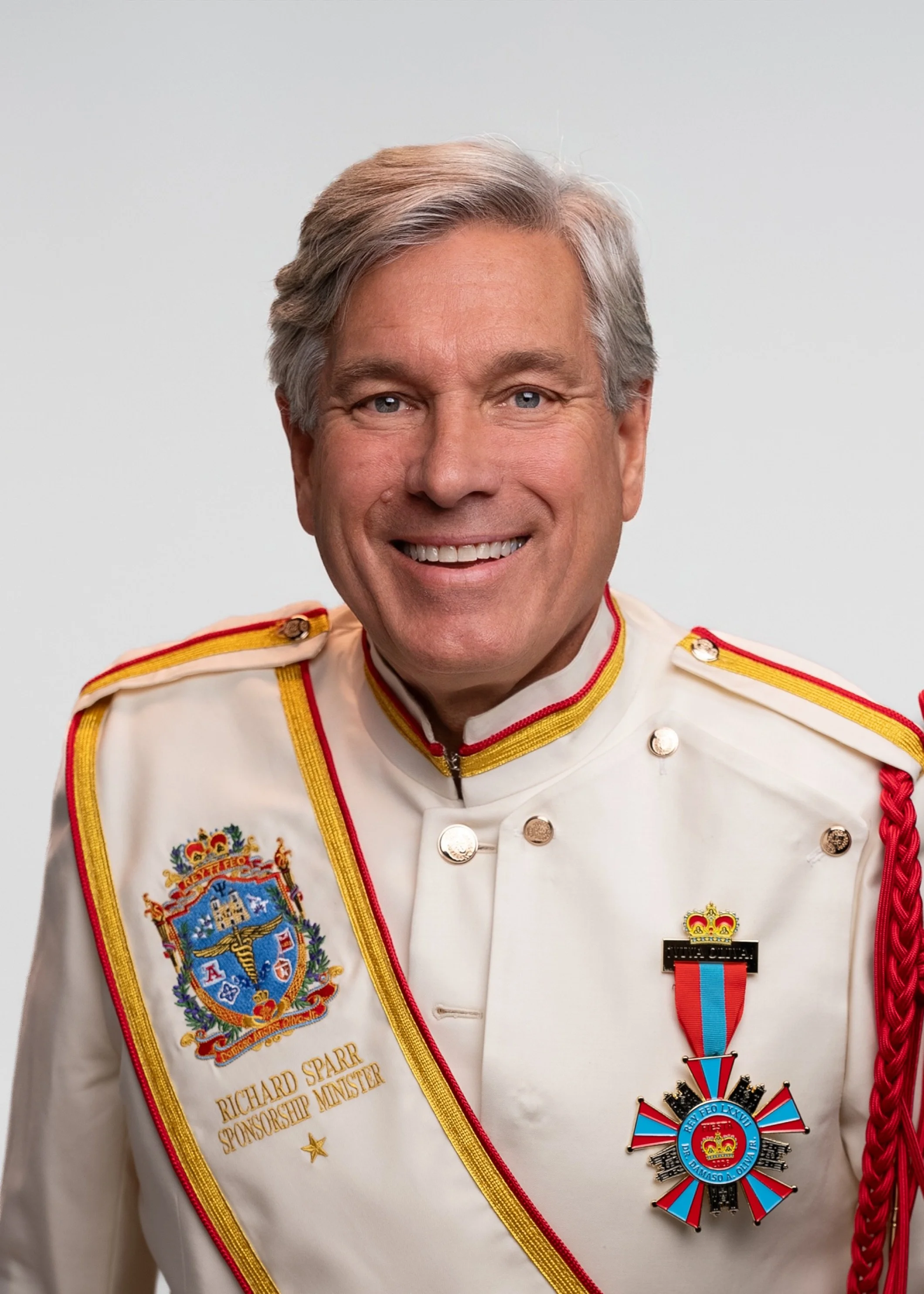 Headshot of a smiling middle-aged man with gray hair and blue eyes, wearing a red button-up shirt, against a plain light gray background.