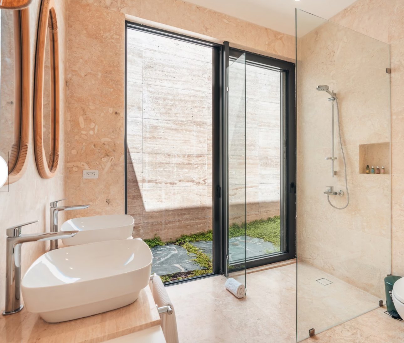 Modern bathroom with double sinks, mirrors, glass shower, and large window.