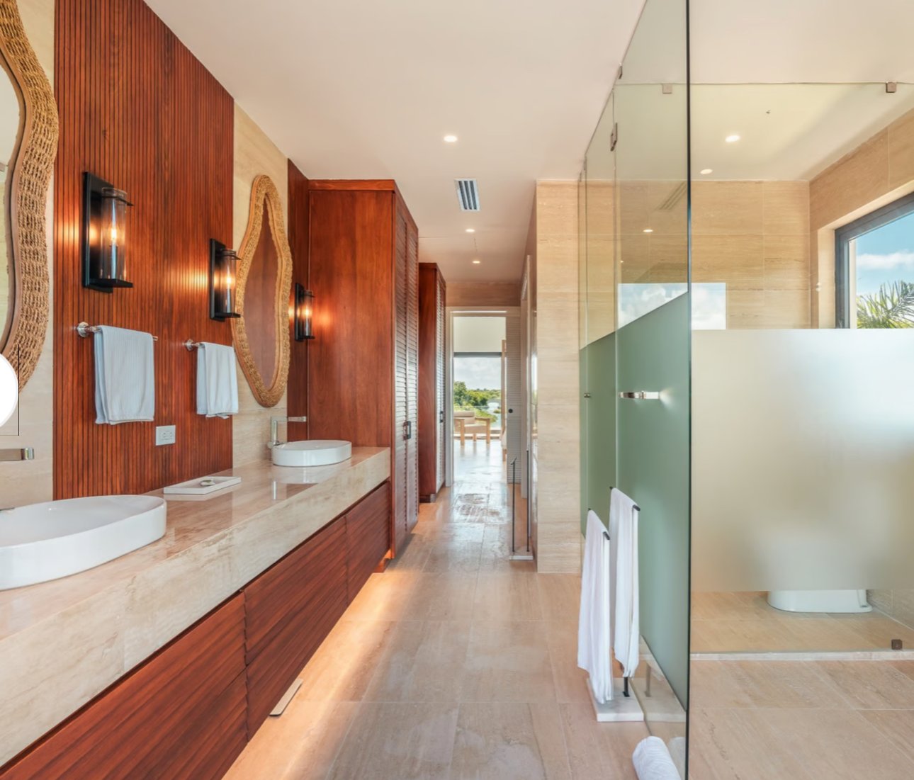 Modern bathroom with dual sinks, large mirrors, wooden paneling, glass-enclosed shower, and natural light from a window.