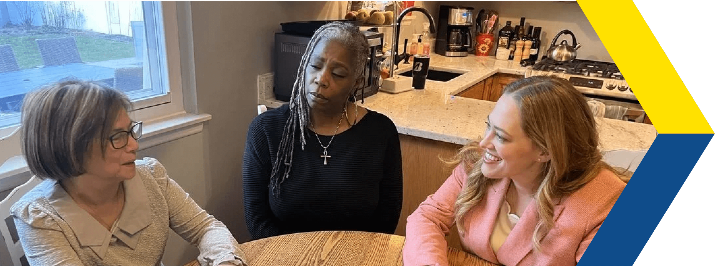Christina and two other people sitting at a wooden table in a kitchen, engaged in conversation.