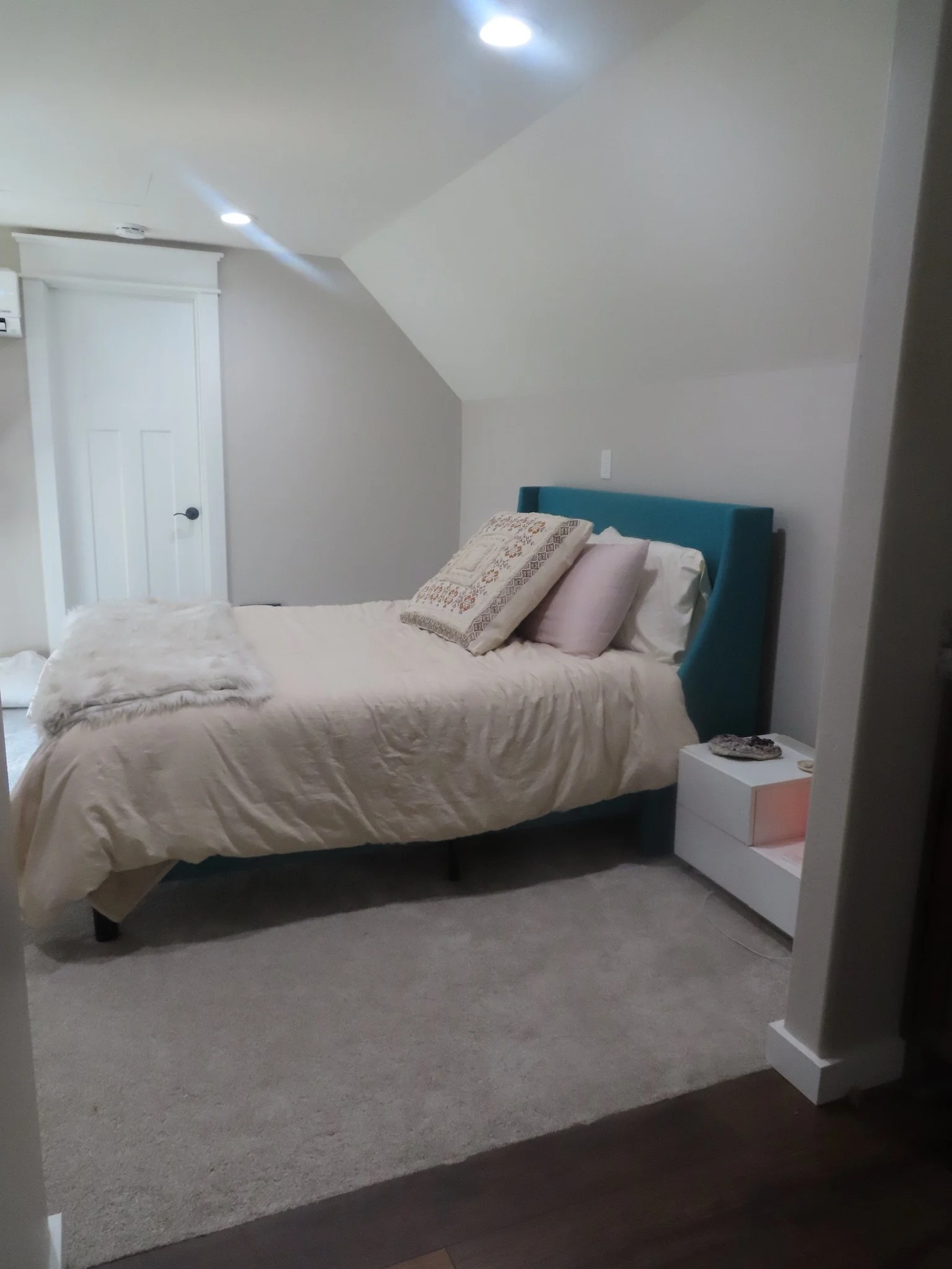 Bedroom with a bed, pillows, and a nightstand under a sloped ceiling, featuring recessed lighting.