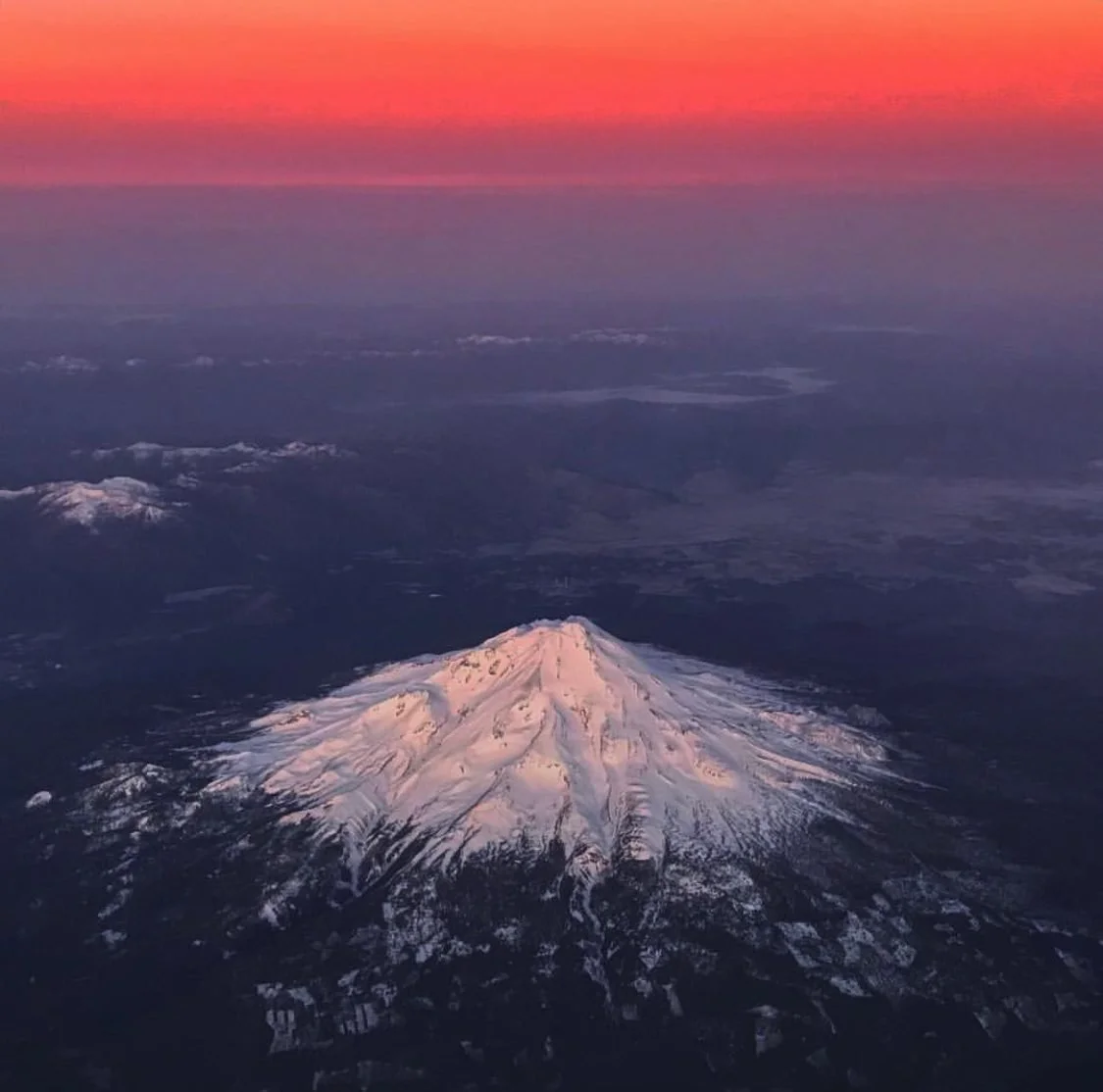 O Monte Shasta visto da janela do avião ao entardecer, acima das nuvens