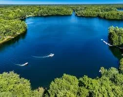 A large body of water surrounded by green trees with two boats sailing on it.