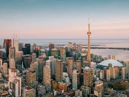 A city skyline featuring tall buildings and a prominent tower, with a body of water nearby during sunset.