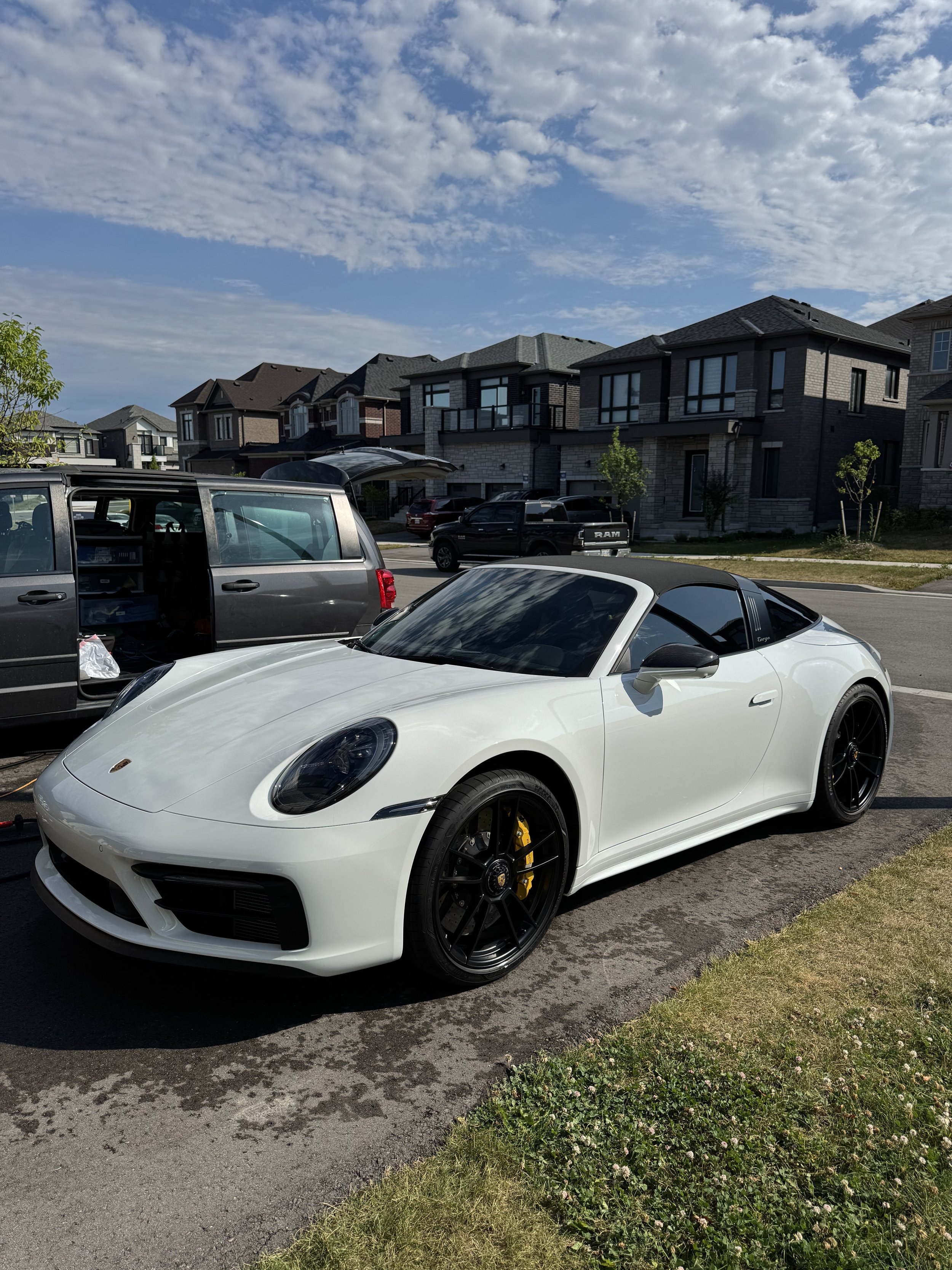 White Porsche sports car parked on a driveway in front of modern houses under a partly cloudy sky.