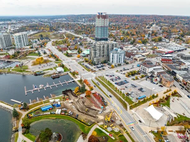 Aerial view of a city with a river, a marina, a park, and various buildings including a tall skyscraper under construction.