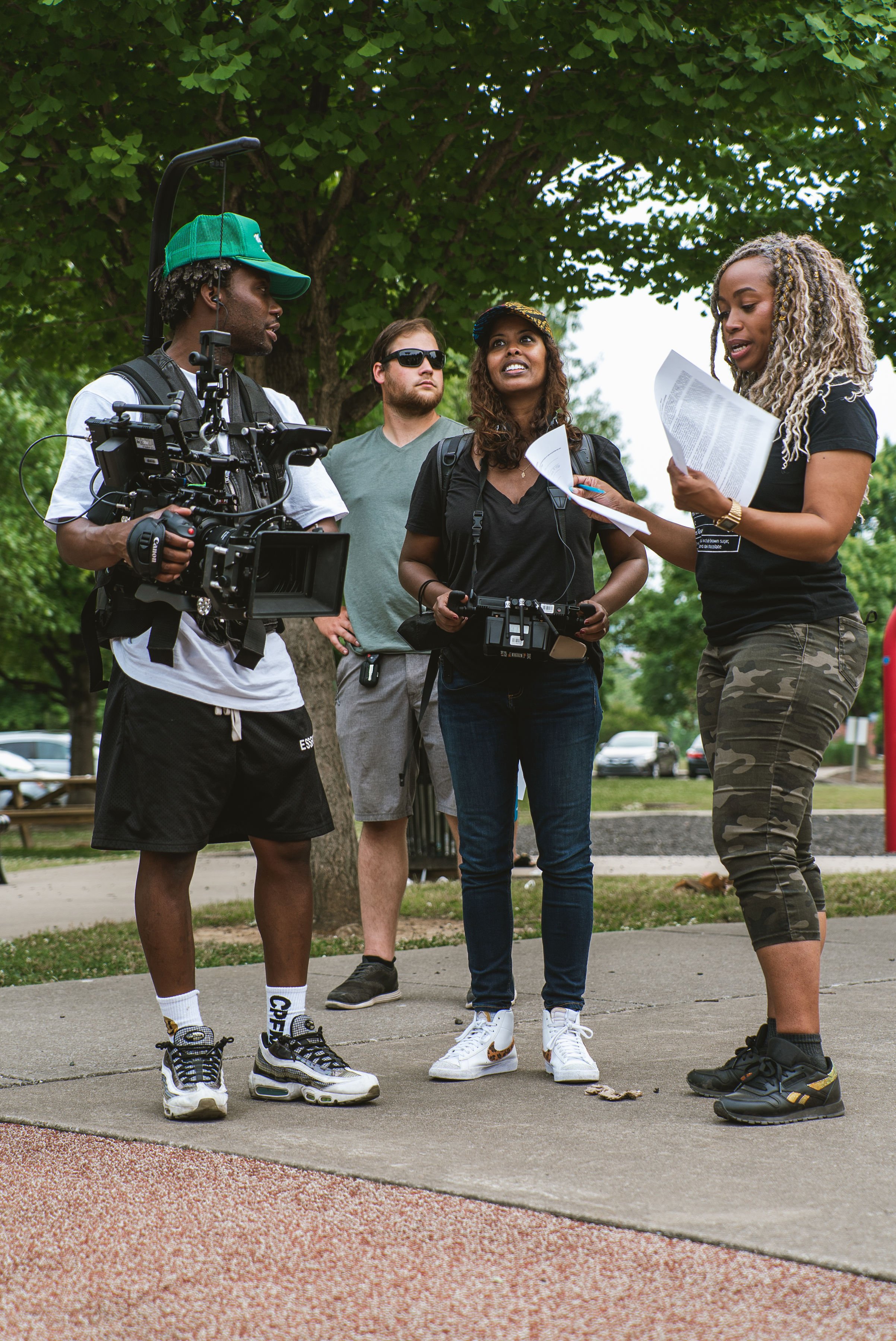Fletch Power with a group of three people in casual clothing standing outdoors; one holding a camera rig, others with papers and camera, discussing or preparing for a film shoot.