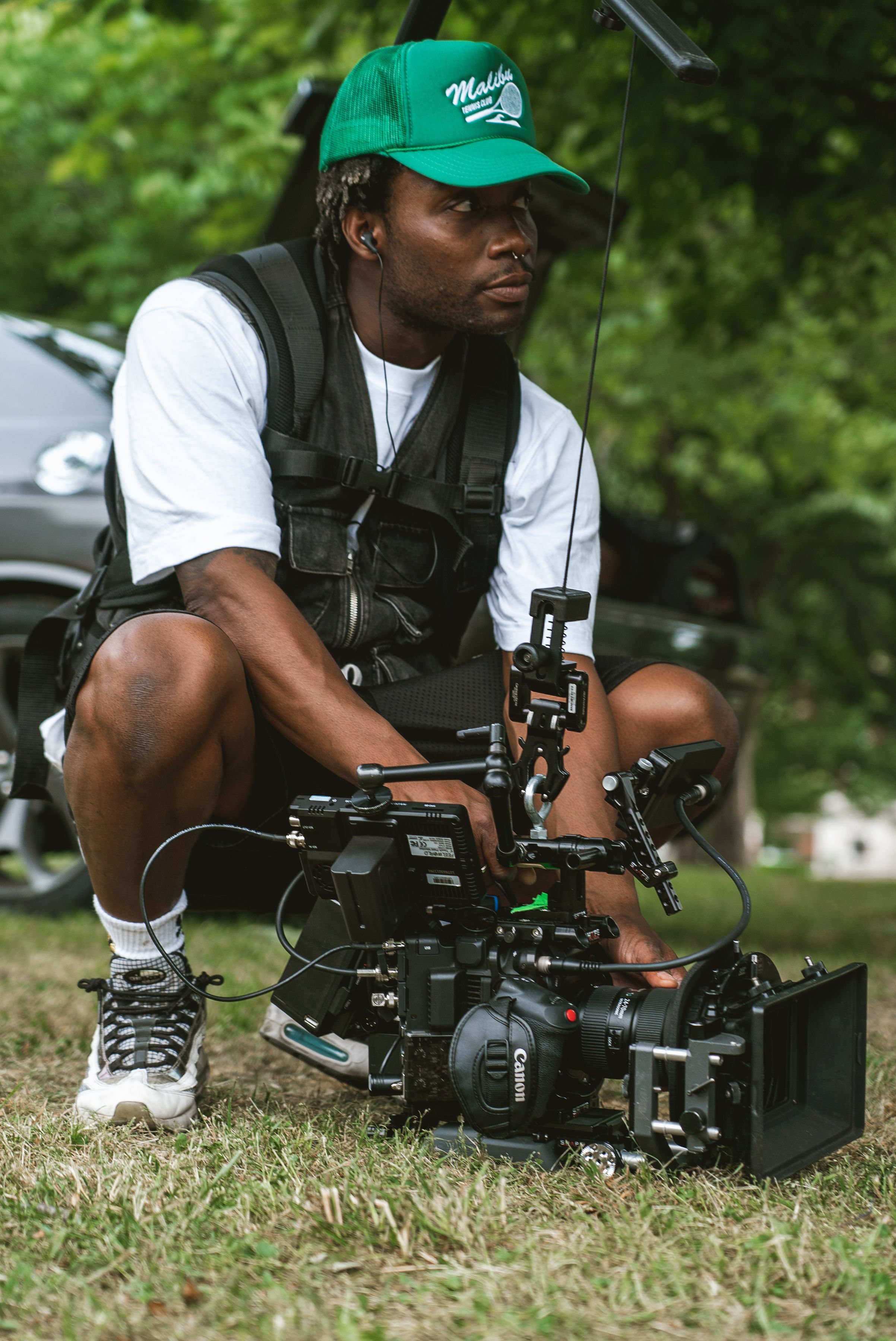 Fletch power wearing a green cap and white shirt operating a Canon video camera outdoors.