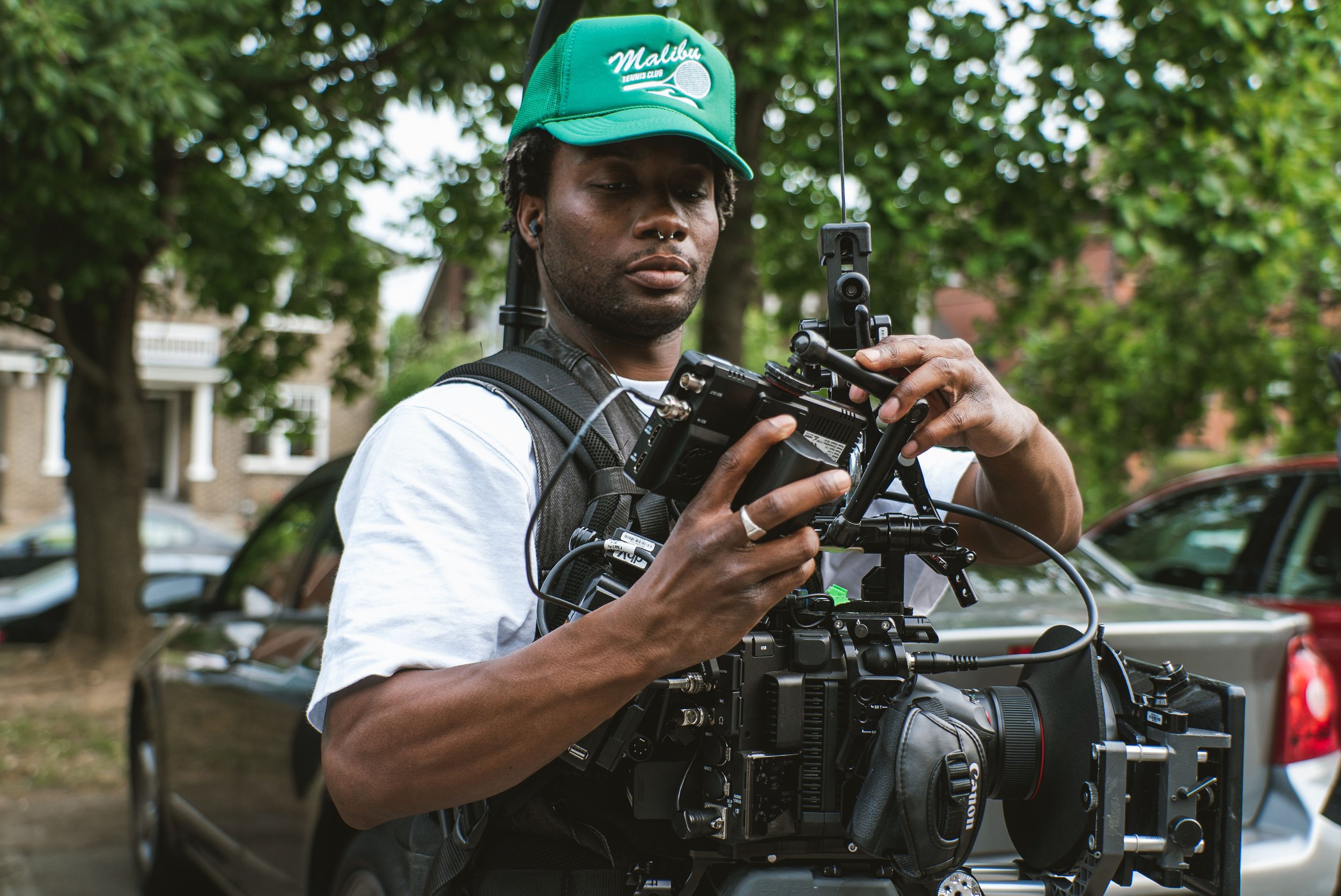 Fletch Power adjusting a professional video camera outdoors on a street with trees and cars in the background.