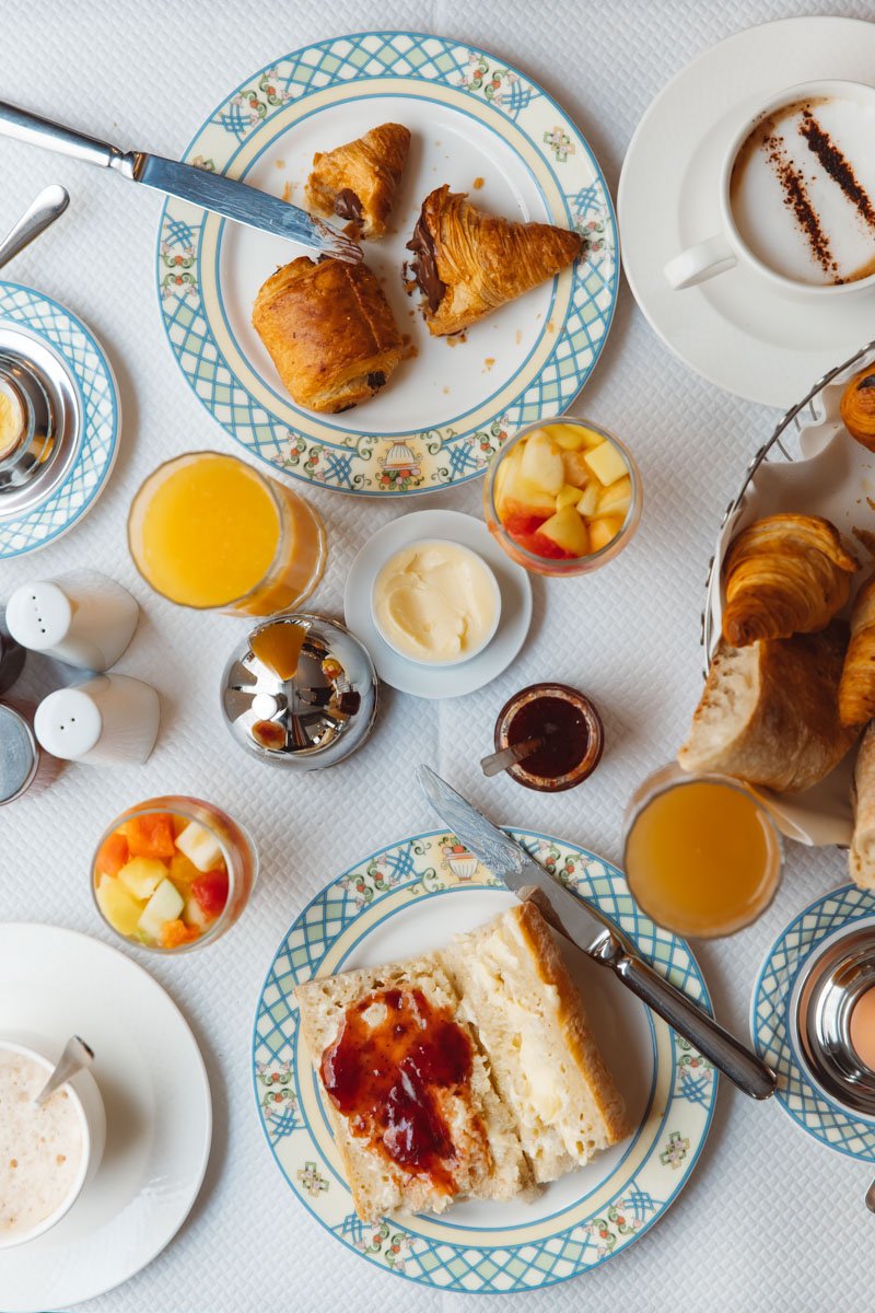 Petit-déjeuner avec croissants, jus d'orange, pain avec confiture, café, fruits frais et beurre sur une table.