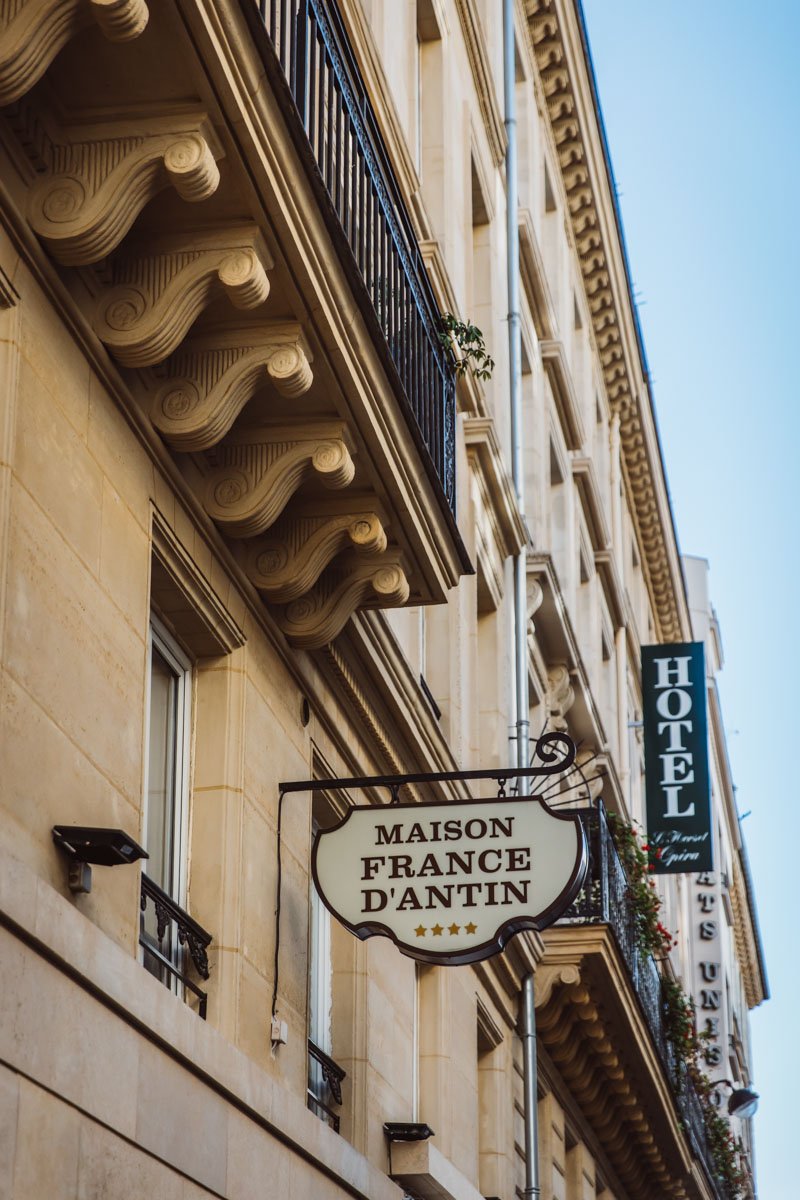 Façade d'un hôtel parisien avec enseignes "Maison France d'Antin" et "Hôtel". Architecture haussmannienne avec balcons en fer forgé.