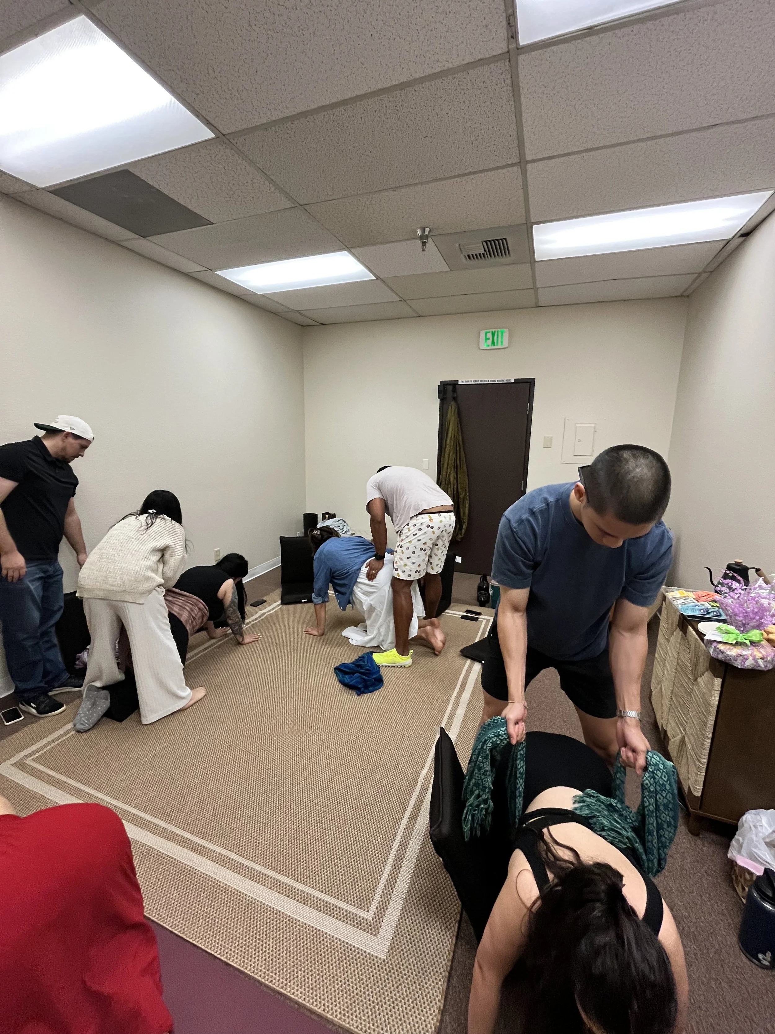 Multiple people in a small room appear to be engaged in a playful or humorous activity, resembling a mock or playful gathering.