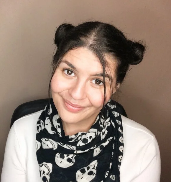 Chloe Forbes-Kindlen with bunny bun hair style, smiling and wearing a white top with black and white skull scarf.