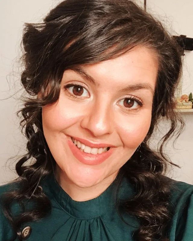 Chloë Forbes-Kindlen, the owner, smiling in her office. Has brown curly hair and green dress on.
