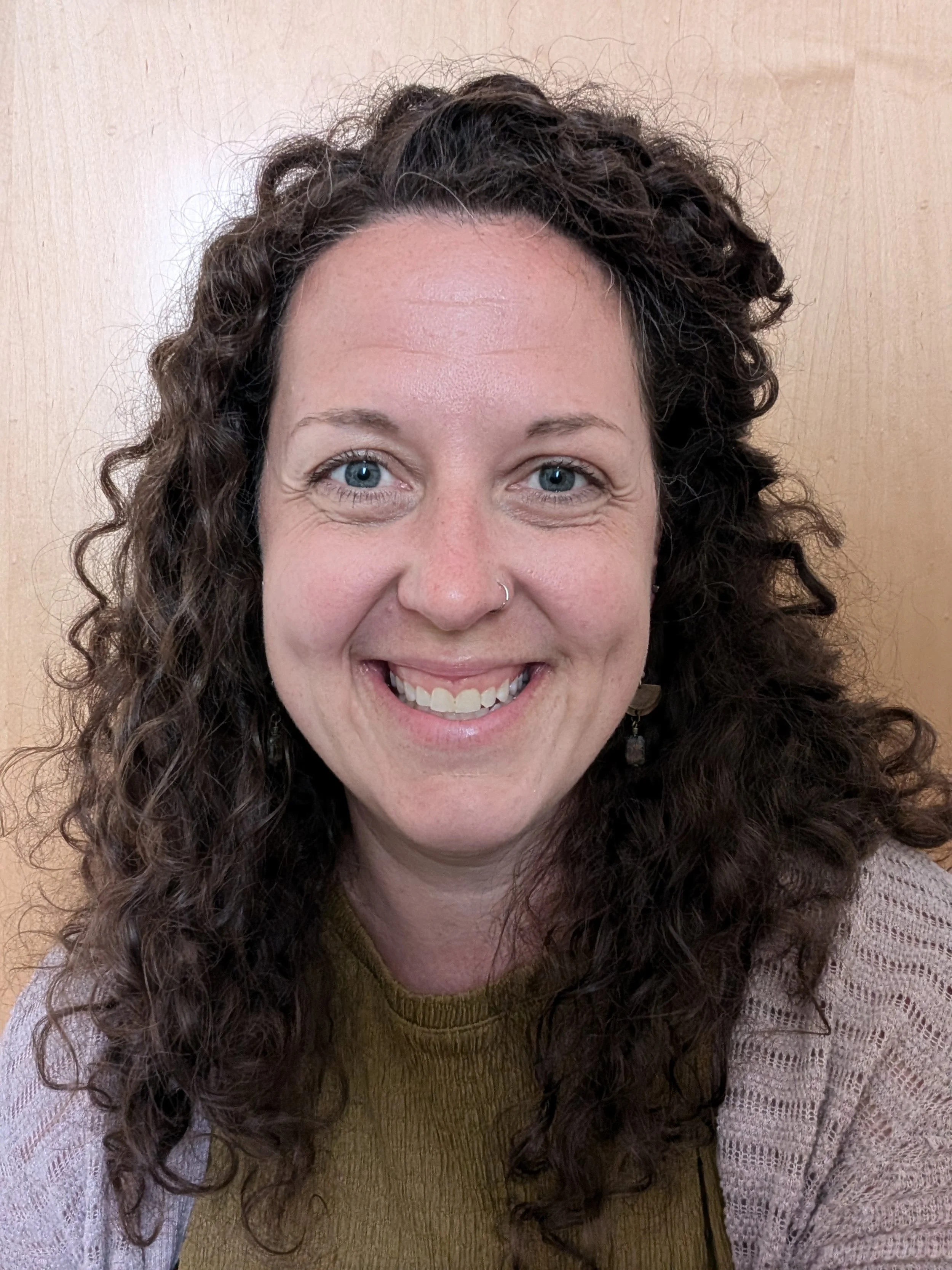 photo of rebekah smiling, she has brown curly hair that falls below her shoulders and she's wearing a green shirt with a beige cardigan