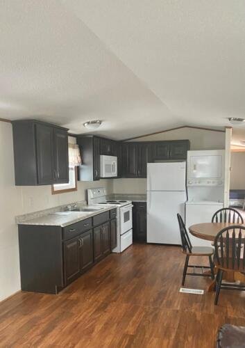 Interior of a kitchen and dining area with dark cabinets, white appliances, and a round dining table with chairs on wood flooring.
