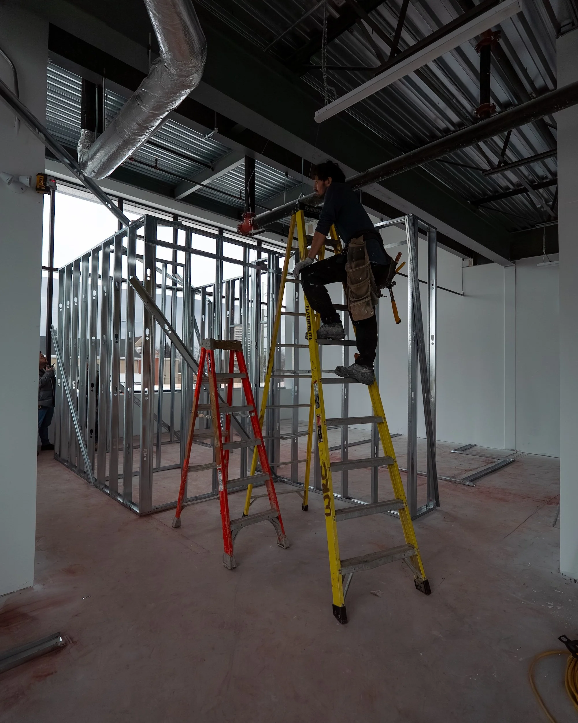 Westrose Construction tradesperson installing steel stud wall framing on a ladder during a commercial office build-out in Toronto