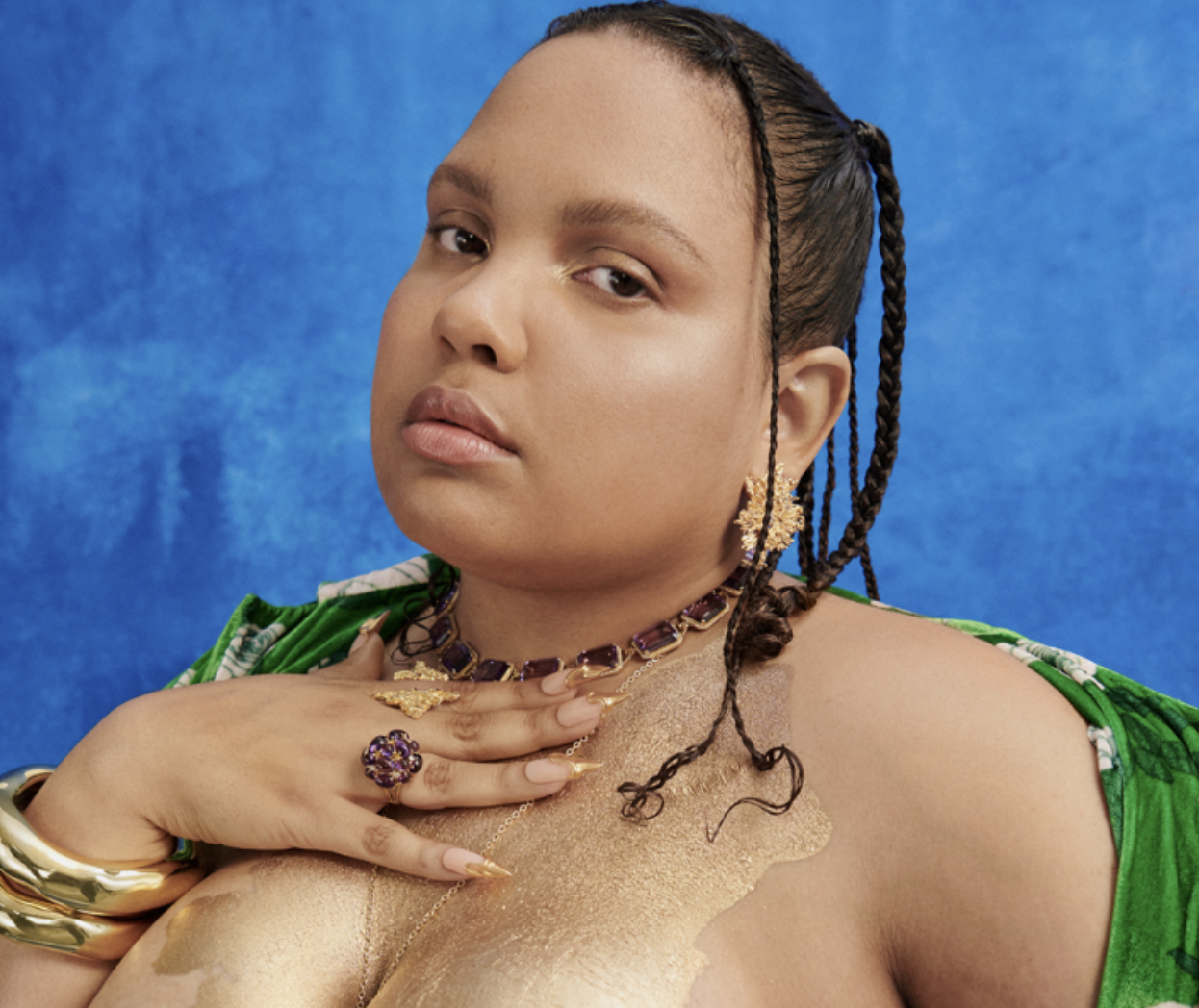 Mariah is a Black queer woman looking at the camera wih gold paint on her chest.