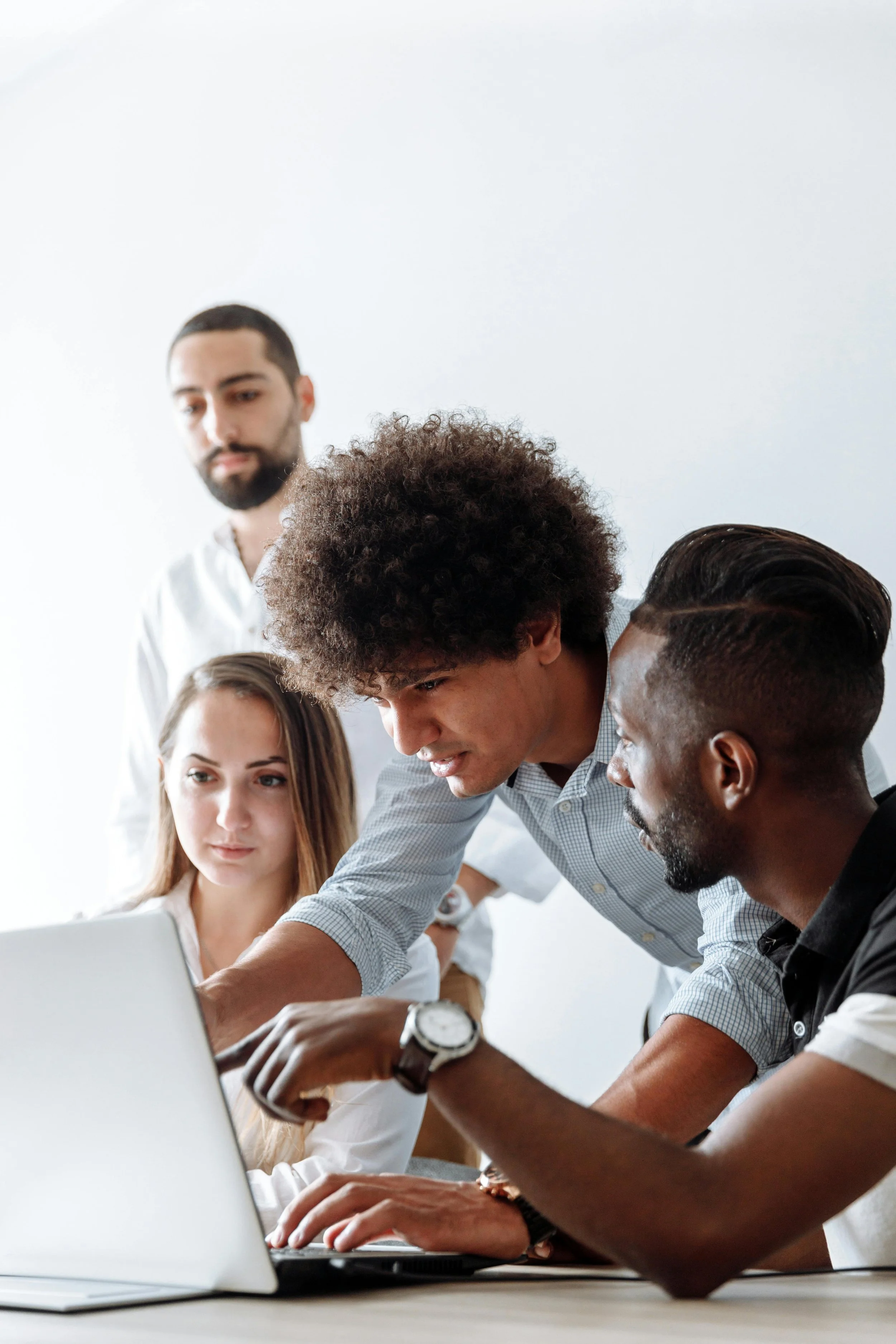 Un grupo de cinco personas colaborando alrededor de una computadora portátil en una oficina moderna.