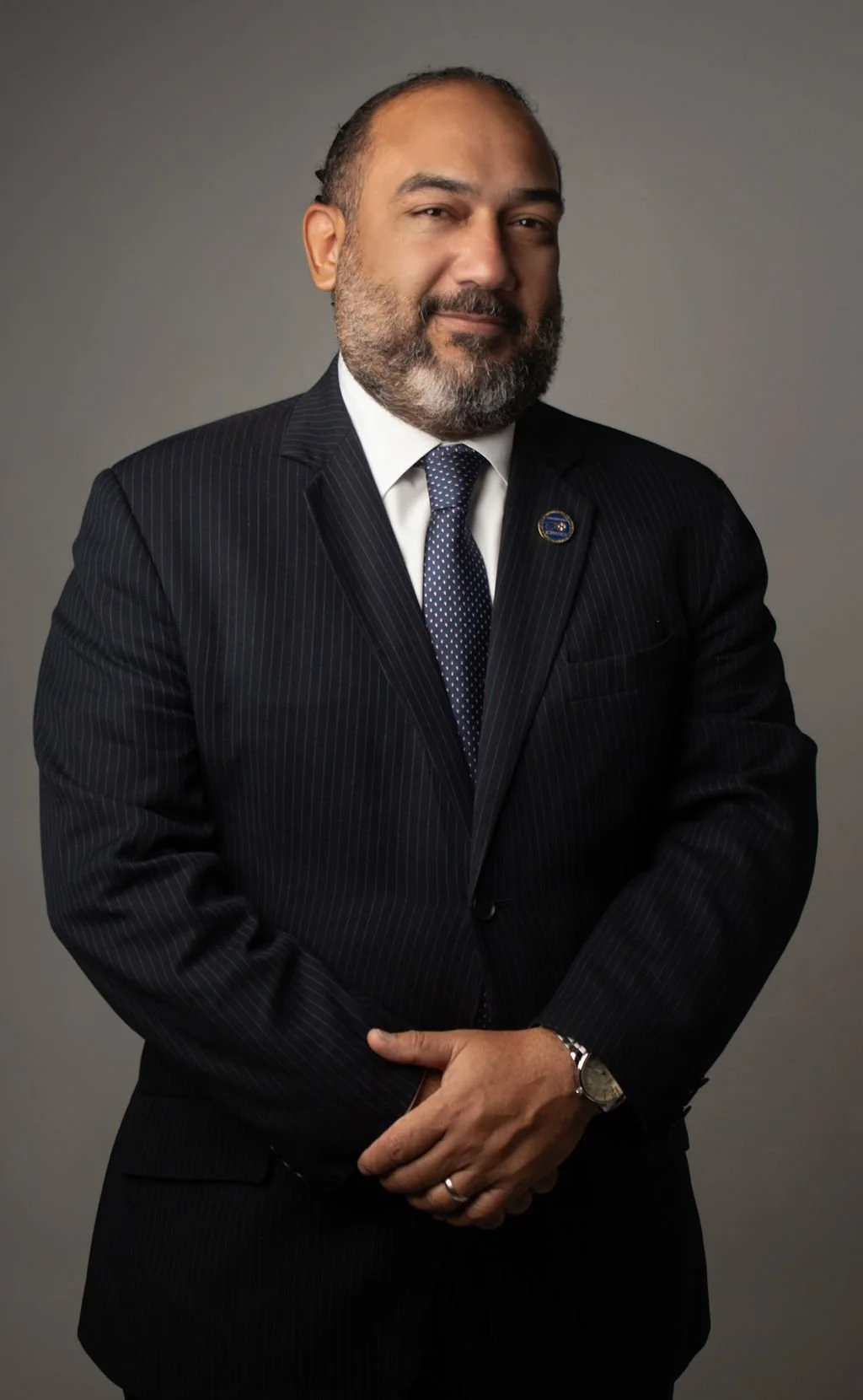 Hombre de negocios con barba, vestida con traje oscuro y corbata con fondo gris.