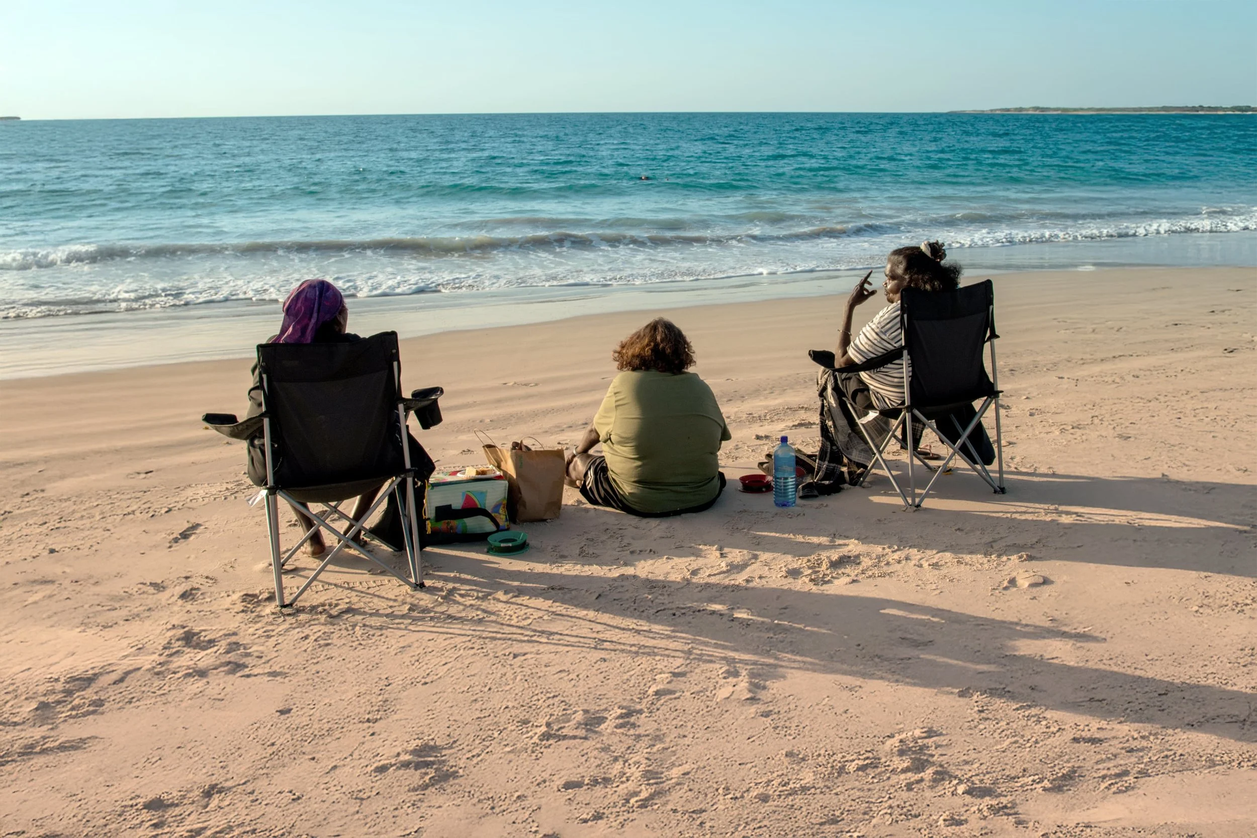 Photo of a group of Indigenous women sitting on a sandy beach at community event.