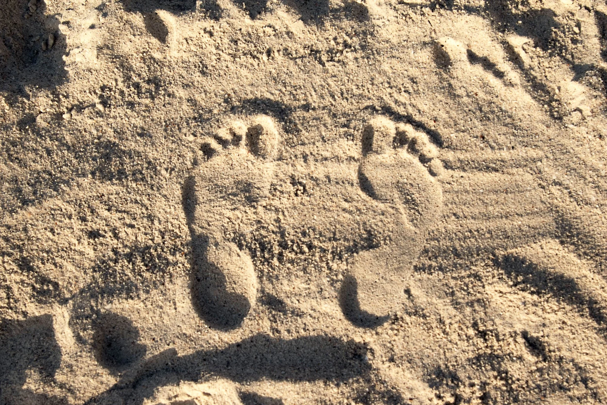 Two human footprints in the sand with a shadow cast over part of them.