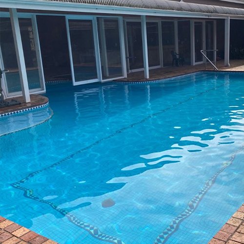 Outdoor swimming pool with clear blue water, surrounded by windows and a brick-paved area.